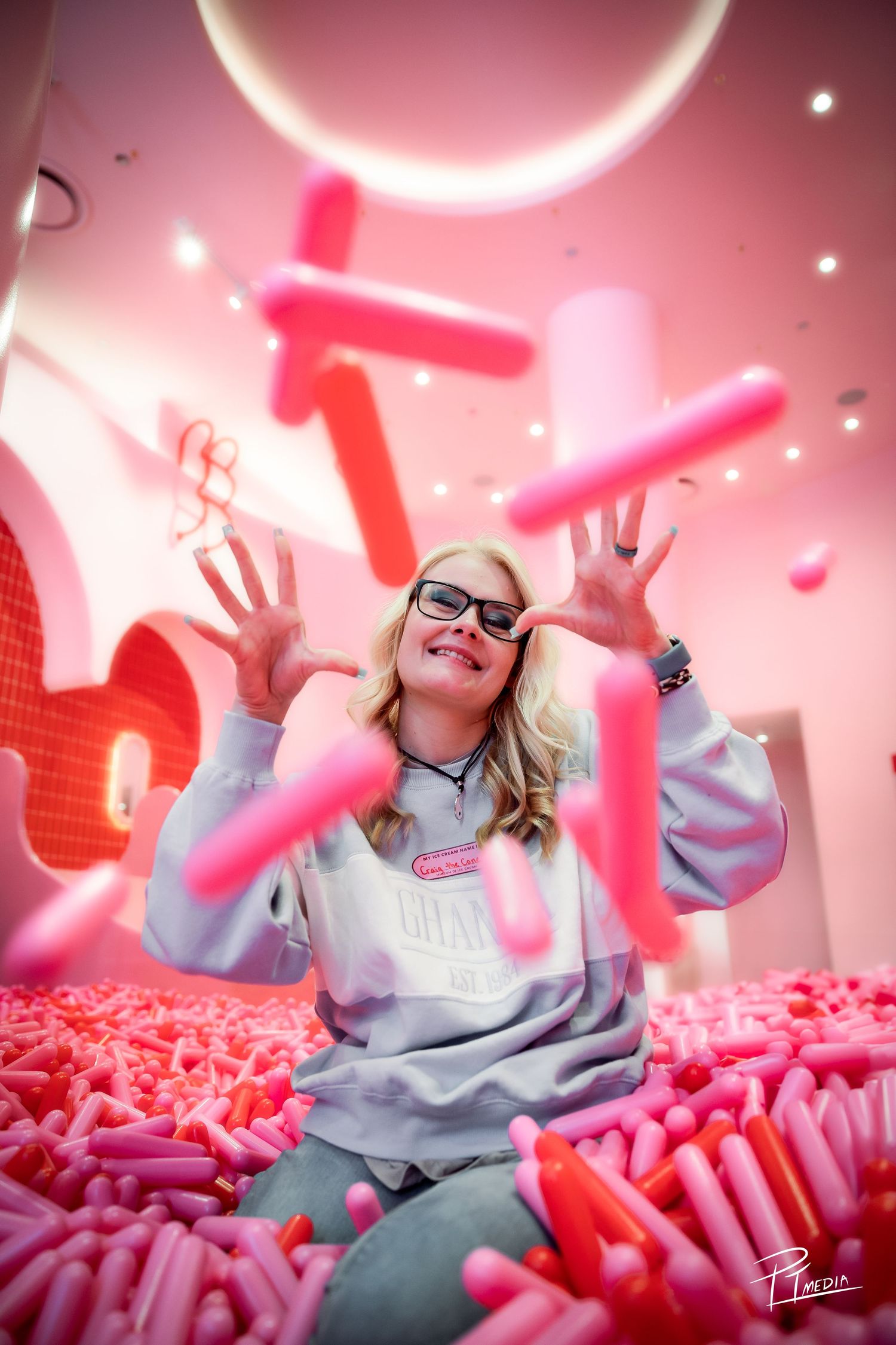 Playful pink-toned scene with floating balloons and a person in a gray sweatshirt surrounded by neon elements.