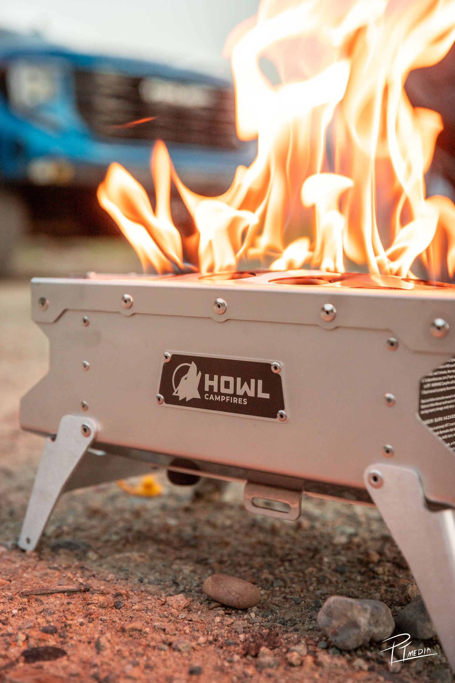 Close-up view of a portable stainless steel fire pit with flames burning through linear holes along its surface.