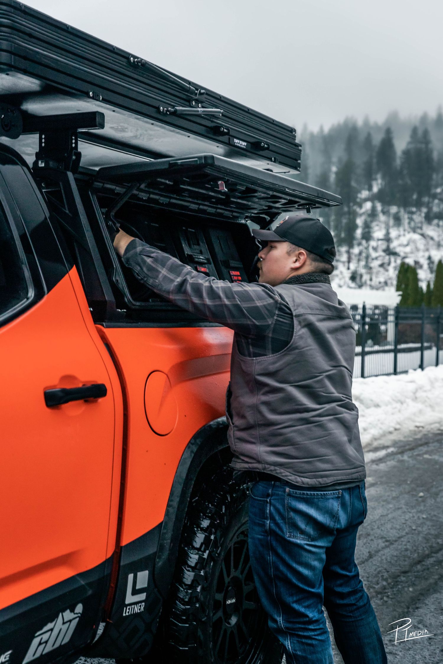 Person in gray jacket opening door of orange vehicle in snowy winter landscape.
