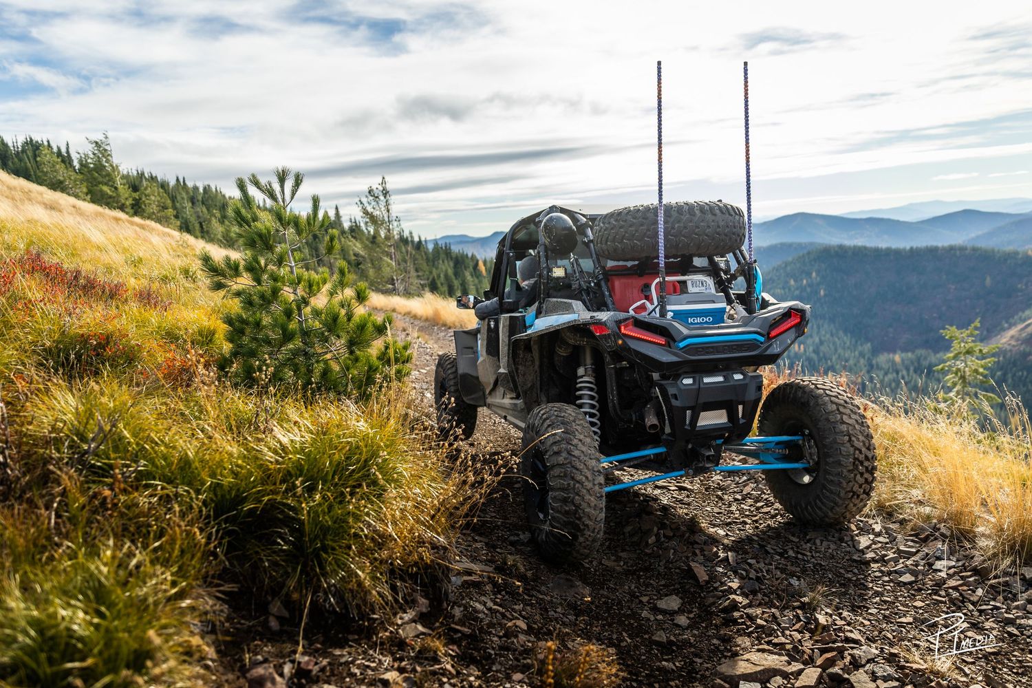 Off-road UTV vehicle with large tires traversing a rugged mountain trail with scenic valley views in the background.