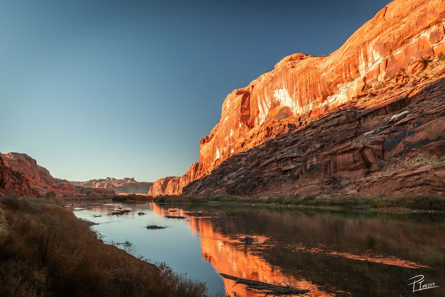 Stunning orange cliffs reflect in calm river waters during sunset at Colorado River in Glen Canyon.