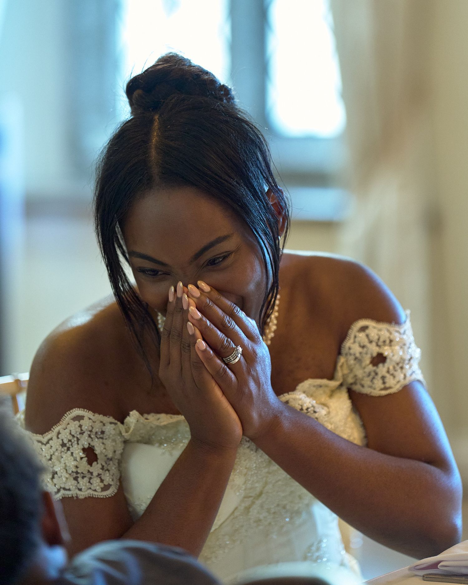 Emotional bride covering her face during a candid wedding moment indoors.