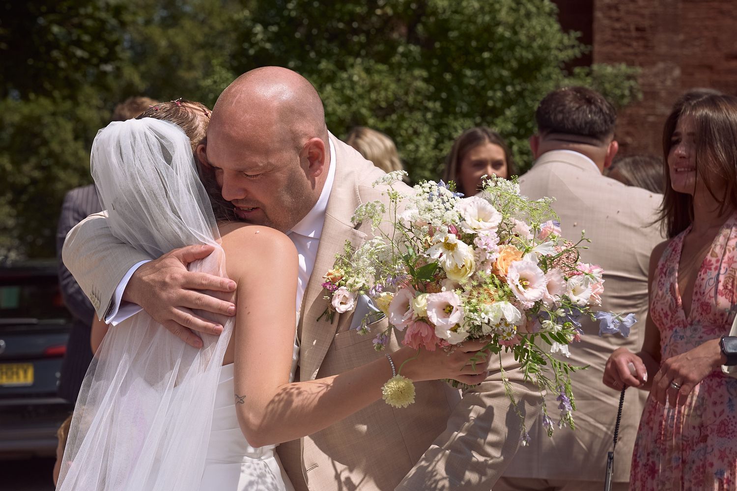 Bride embracing a guest outdoors while holding her wedding bouquet.