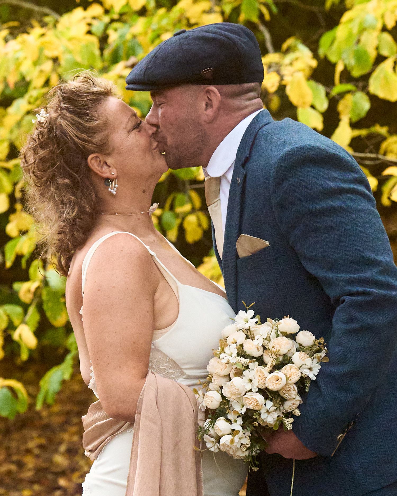 Bride and groom sharing a kiss outdoors while holding a cream bridal bouquet.