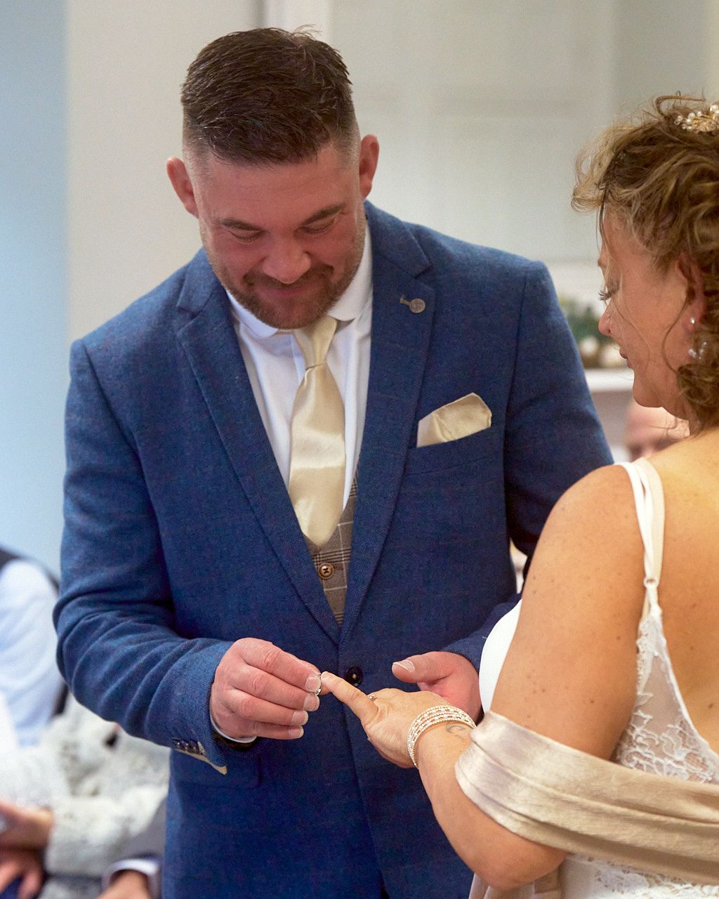 Groom wearing a navy suit putting a wedding ring on his bride's finger during the wedding ceremony.