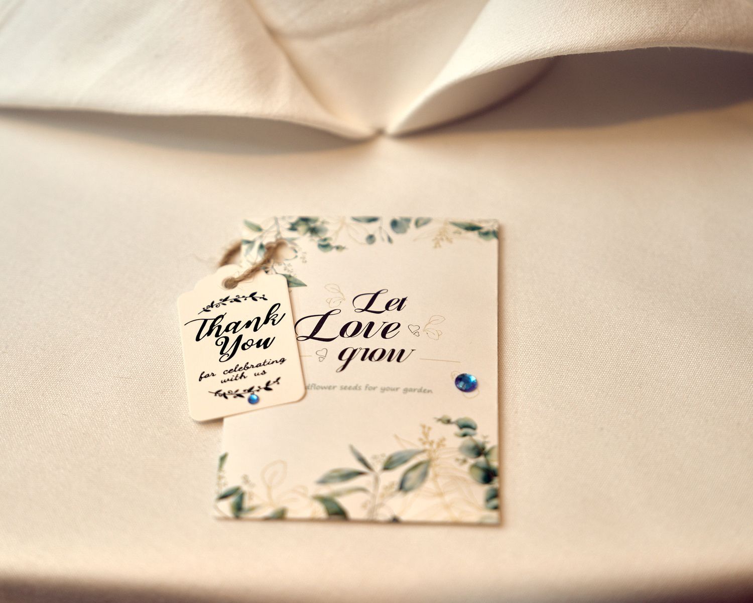 Wedding thank you card and Let Love Grow seed packet favor on white linen tablecloth.