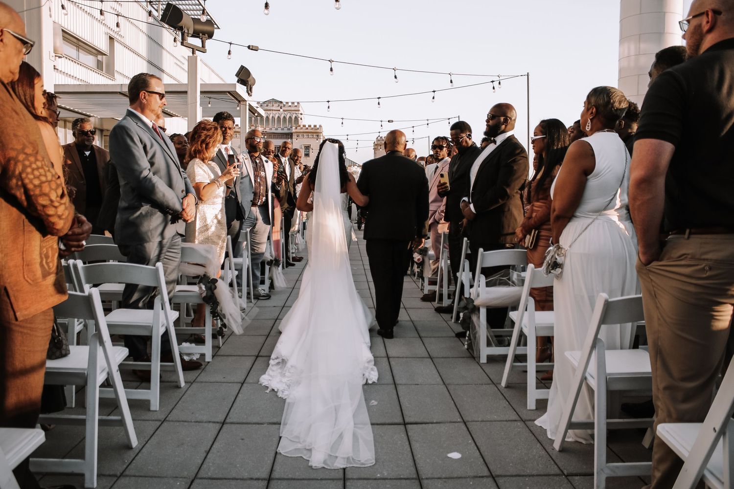 Rows of white chairs set up for an outdoor wedding ceremony with string lights overhead.