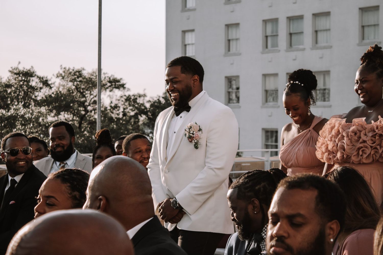 Wedding party members in white tuxedo jackets gathered outside urban building.