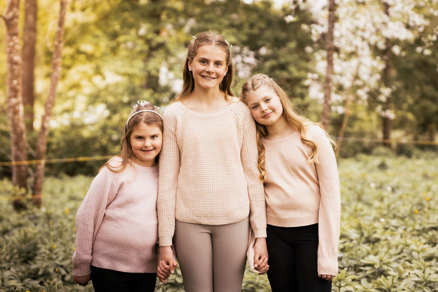 A group in pink and beige outfits poses together outdoors in a wooded setting during autumn.