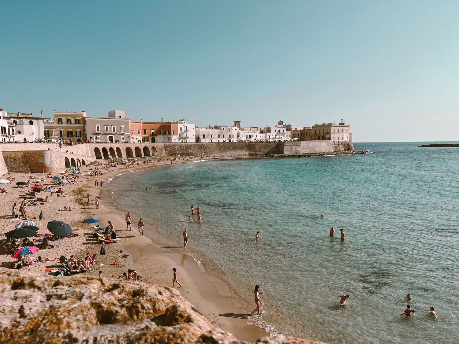 Panoramic beach scene with people enjoying the Mediterranean shoreline on a sunny day.