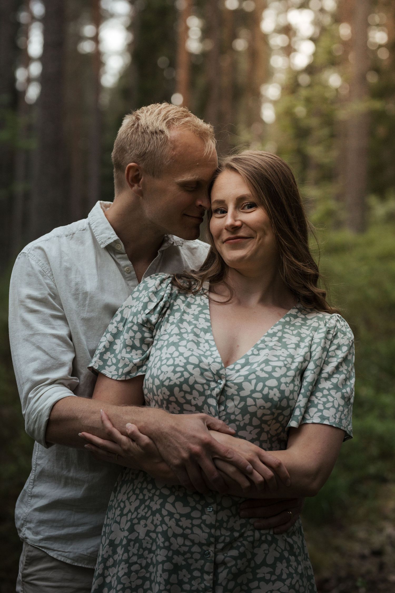 A couple sharing an intimate embrace among tall pine trees in a forest.