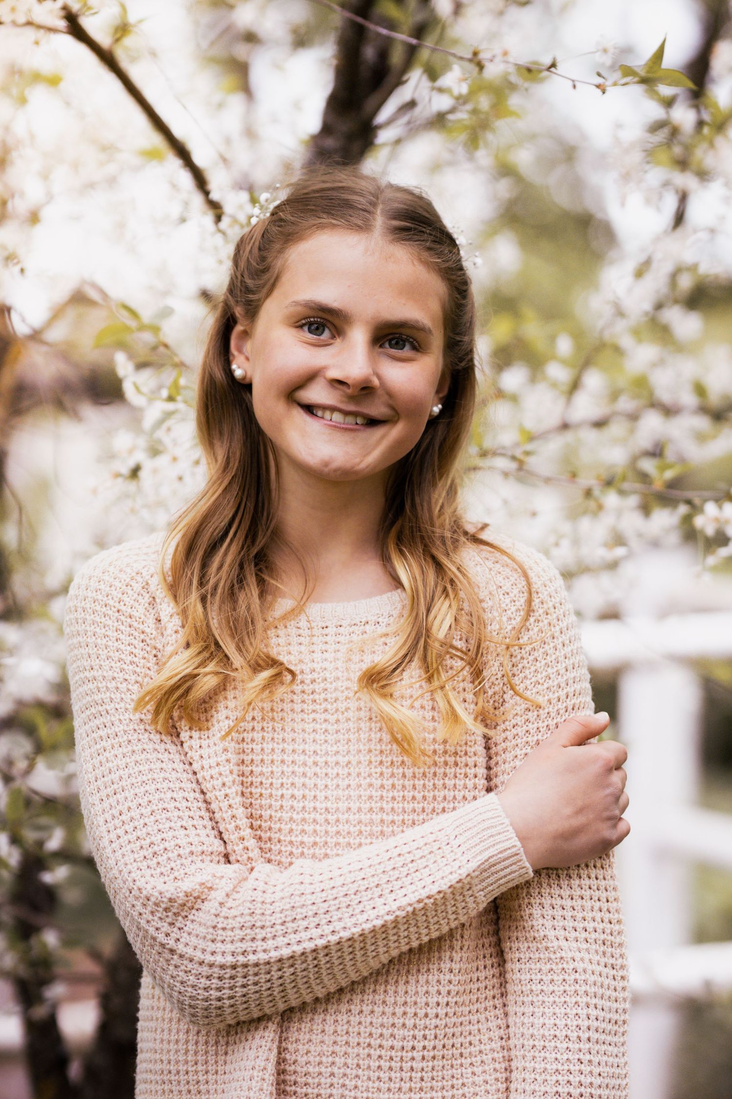 Someone wearing a cozy cream knit sweater poses outdoors among blooming spring cherry blossoms.