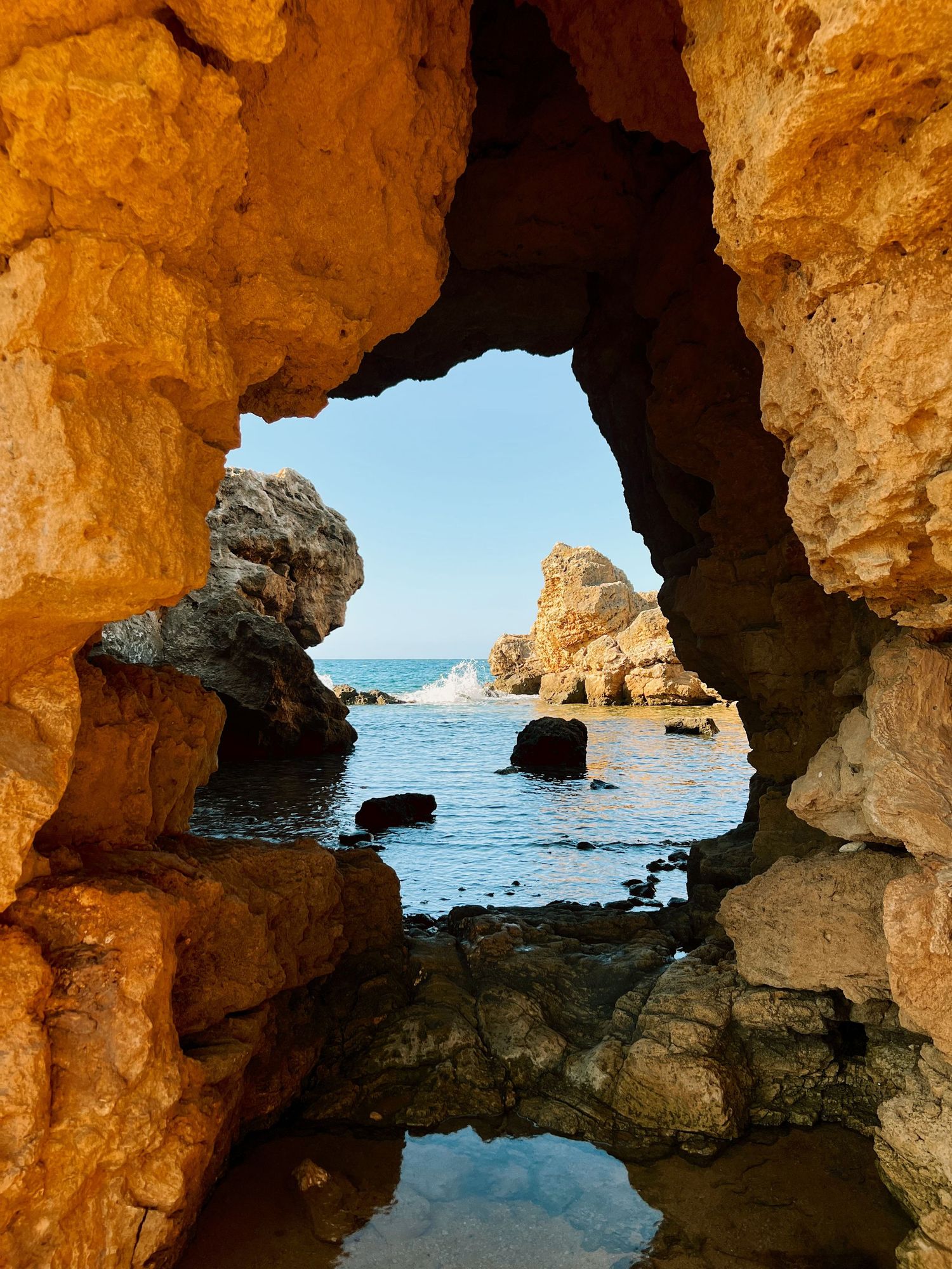 Natural rock arches along a Mediterranean coastline create windows to the blue sea and rocky outcrops.