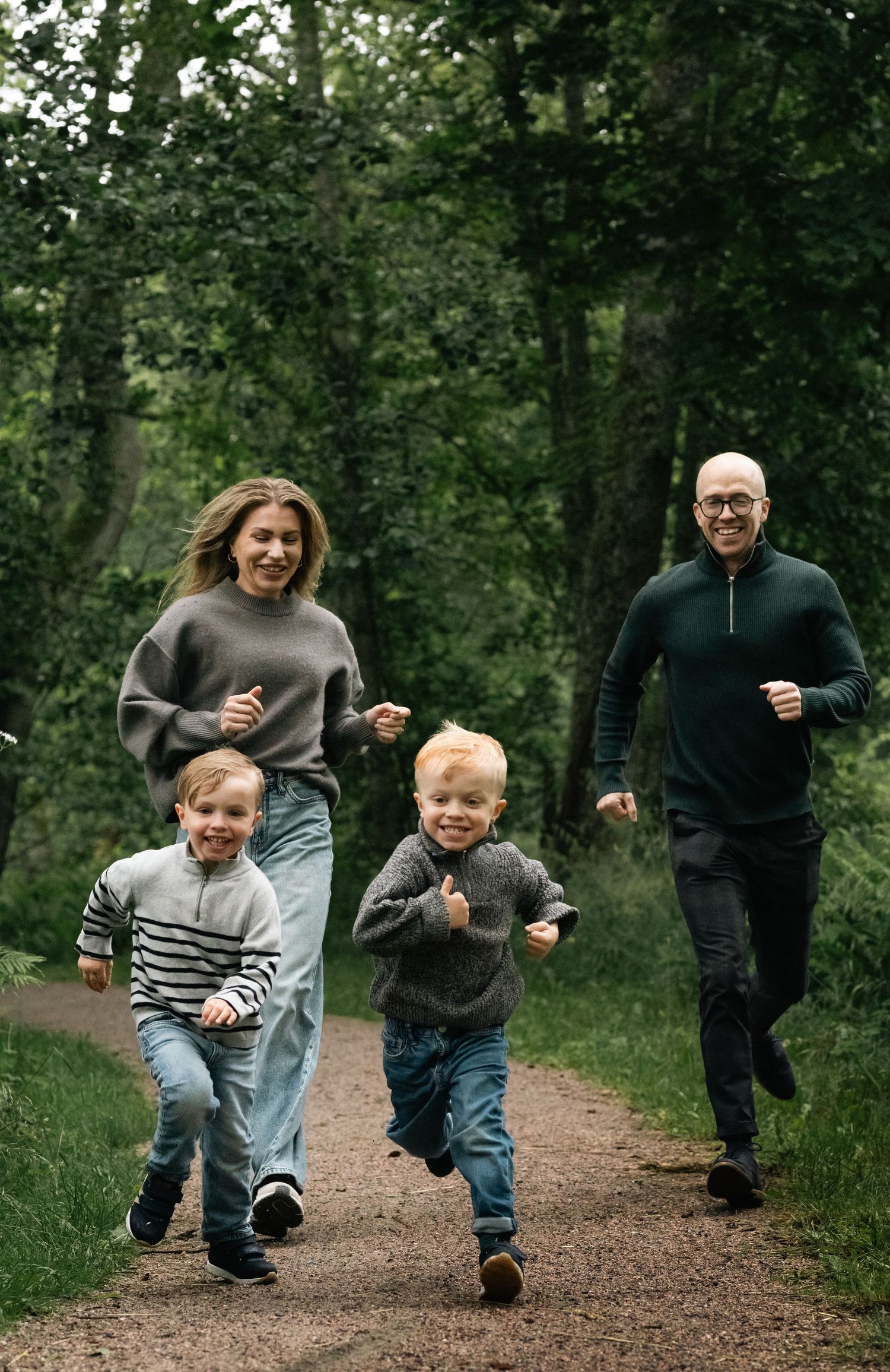 Children running joyfully down a forest trail with adults following behind.