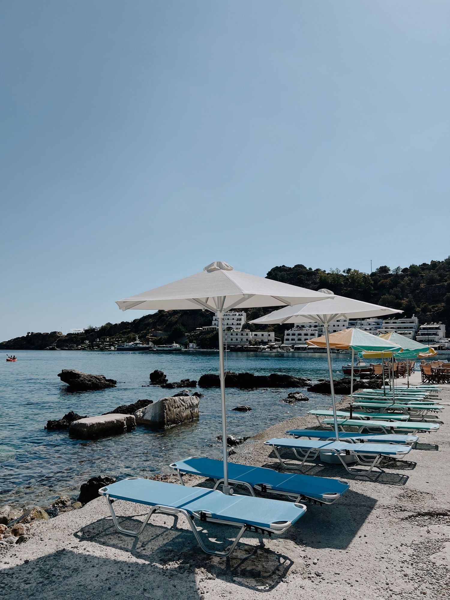 Beach lounge chairs and umbrellas set up on rocky Mediterranean coastline.