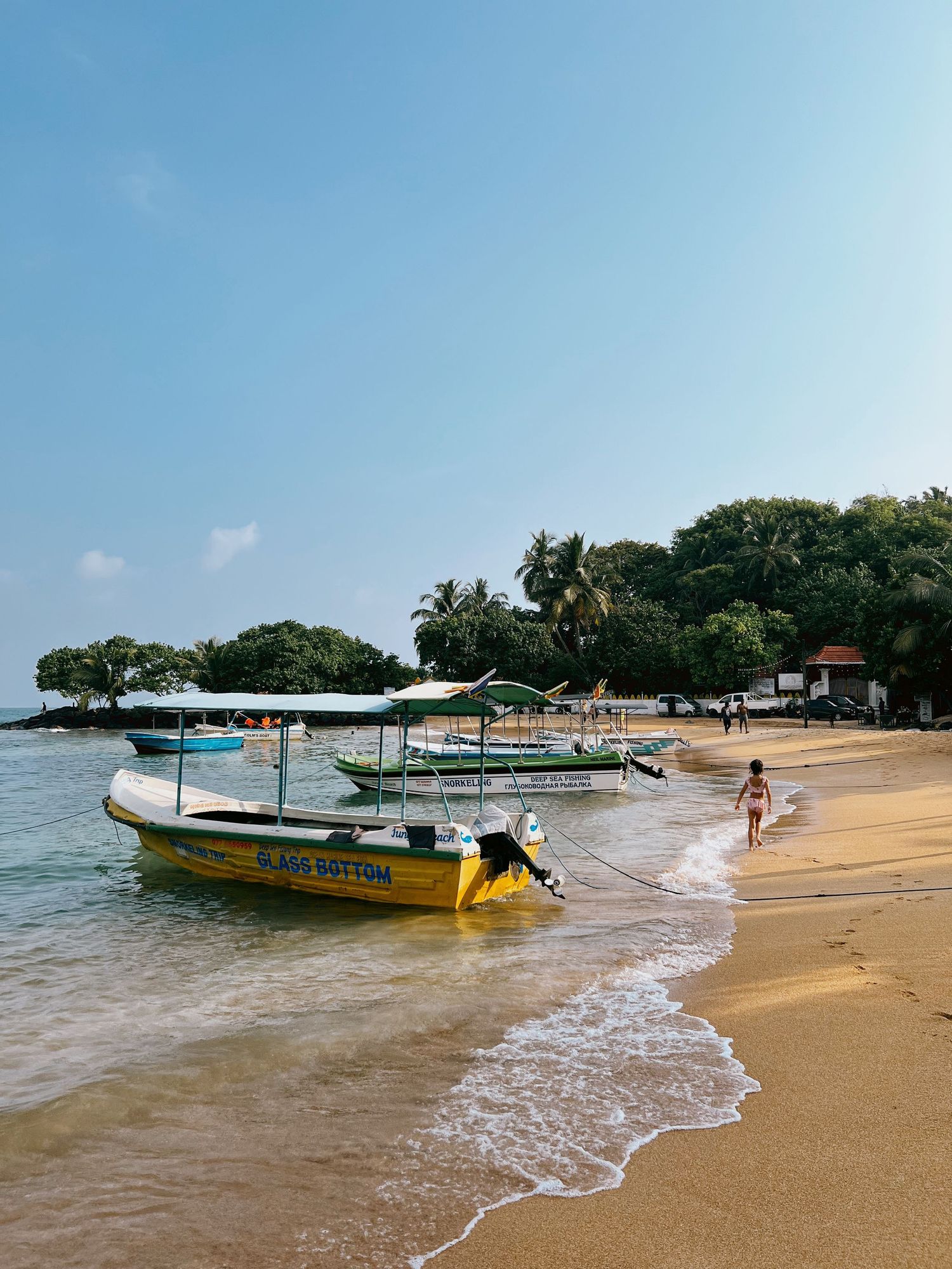 Small boats moored on a sandy beach with palm trees in the background.