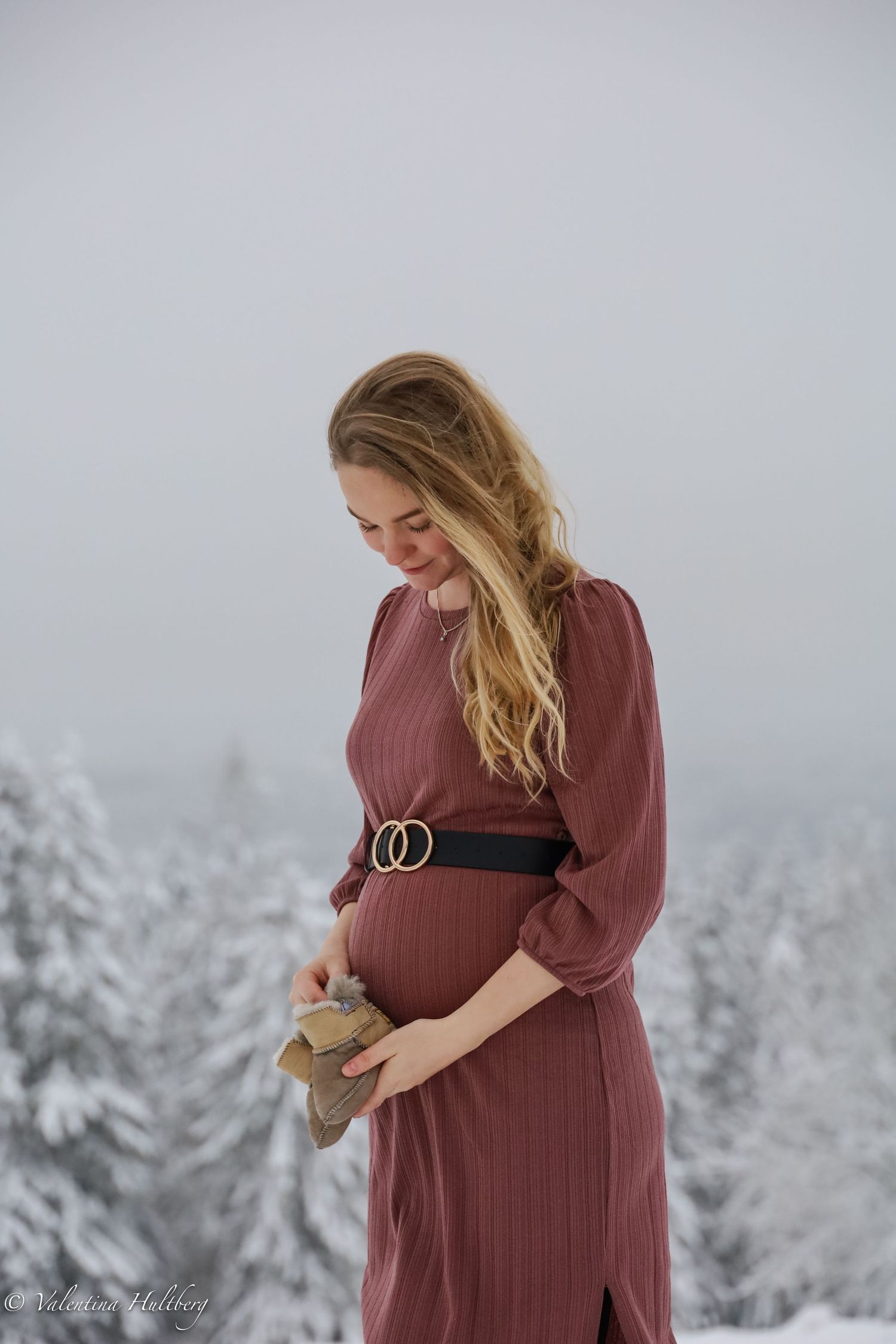 A woman in a mauve dress poses against a snowy winter landscape.