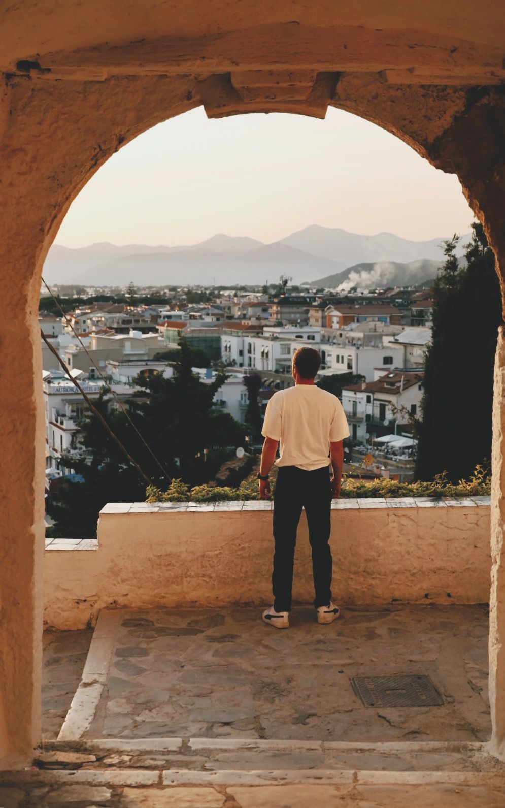 Stone archway framing a panoramic view of a Mediterranean town at sunset.