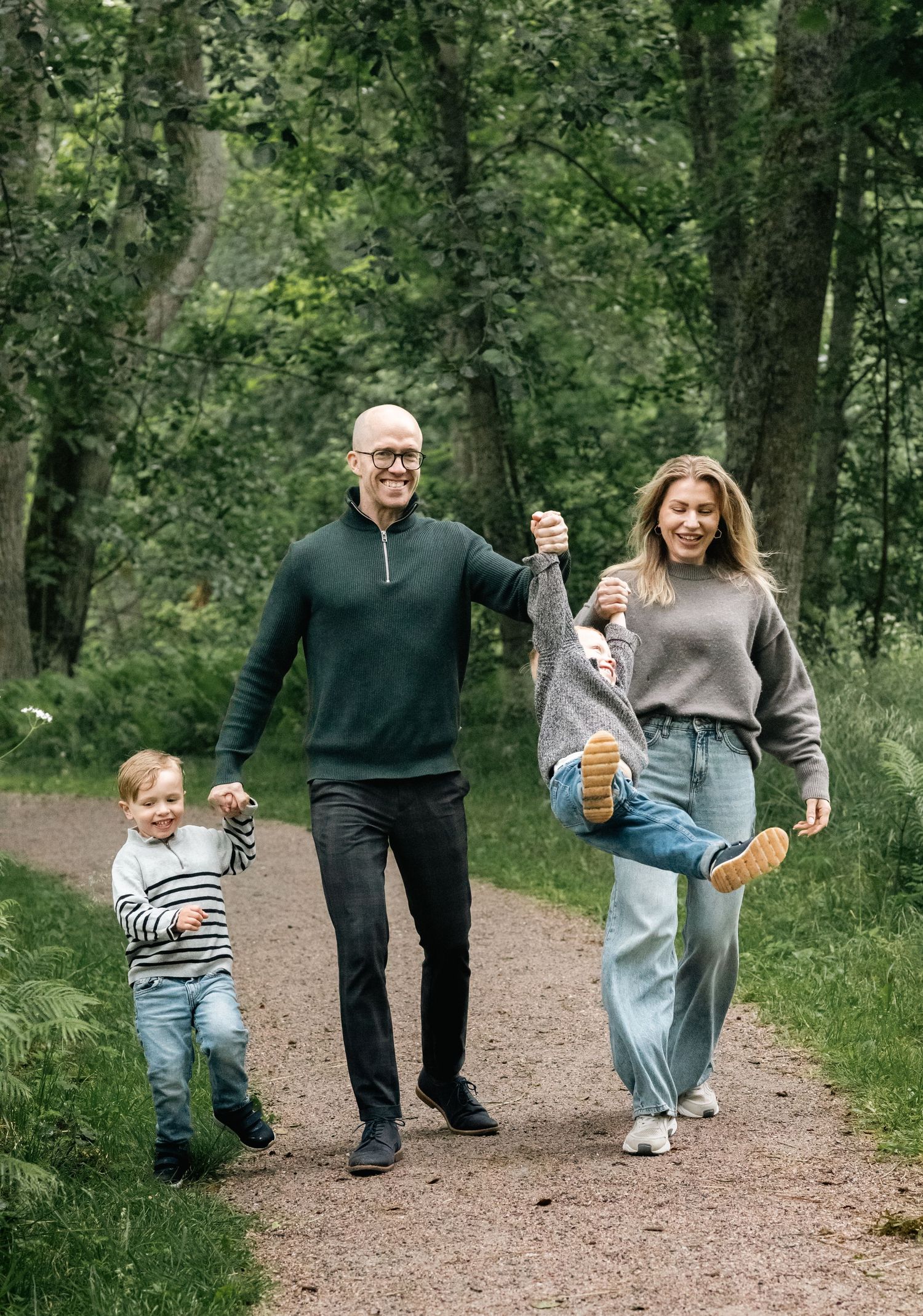 Family walking and playing together on a wooded nature trail in casual attire.