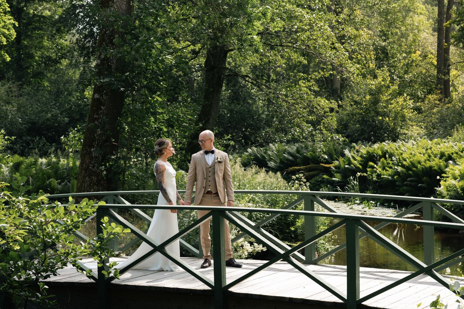 Wedding party stands on a rustic wooden bridge surrounded by lush green trees.