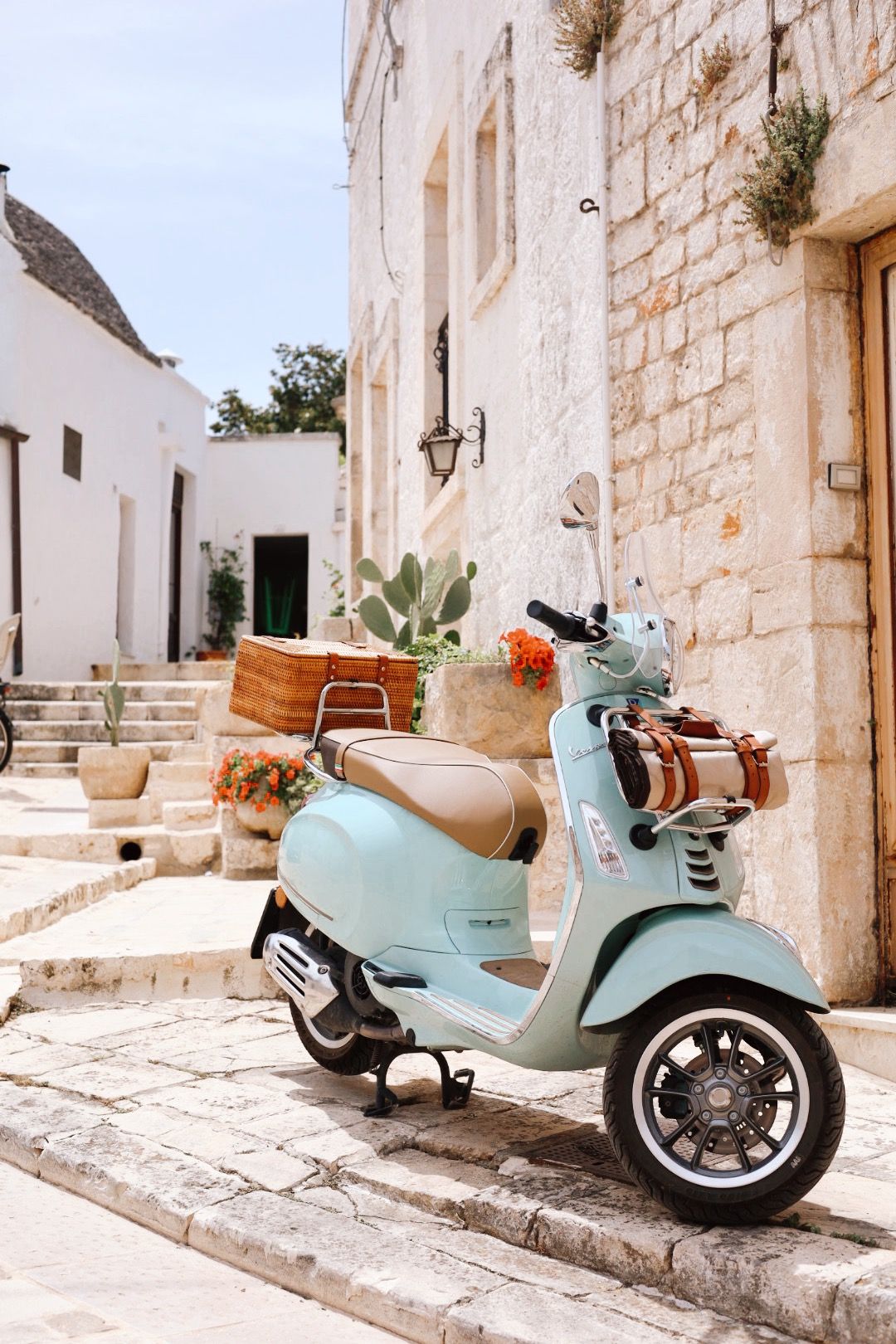 Vintage mint green Vespa scooter parked on cobblestone street against white Mediterranean architecture.