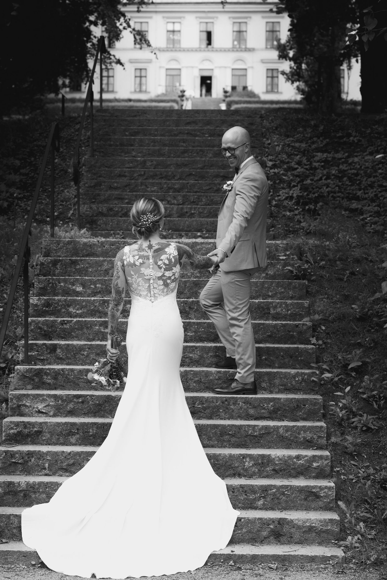 Elegant couple poses on grand stone steps in front of historic white building.