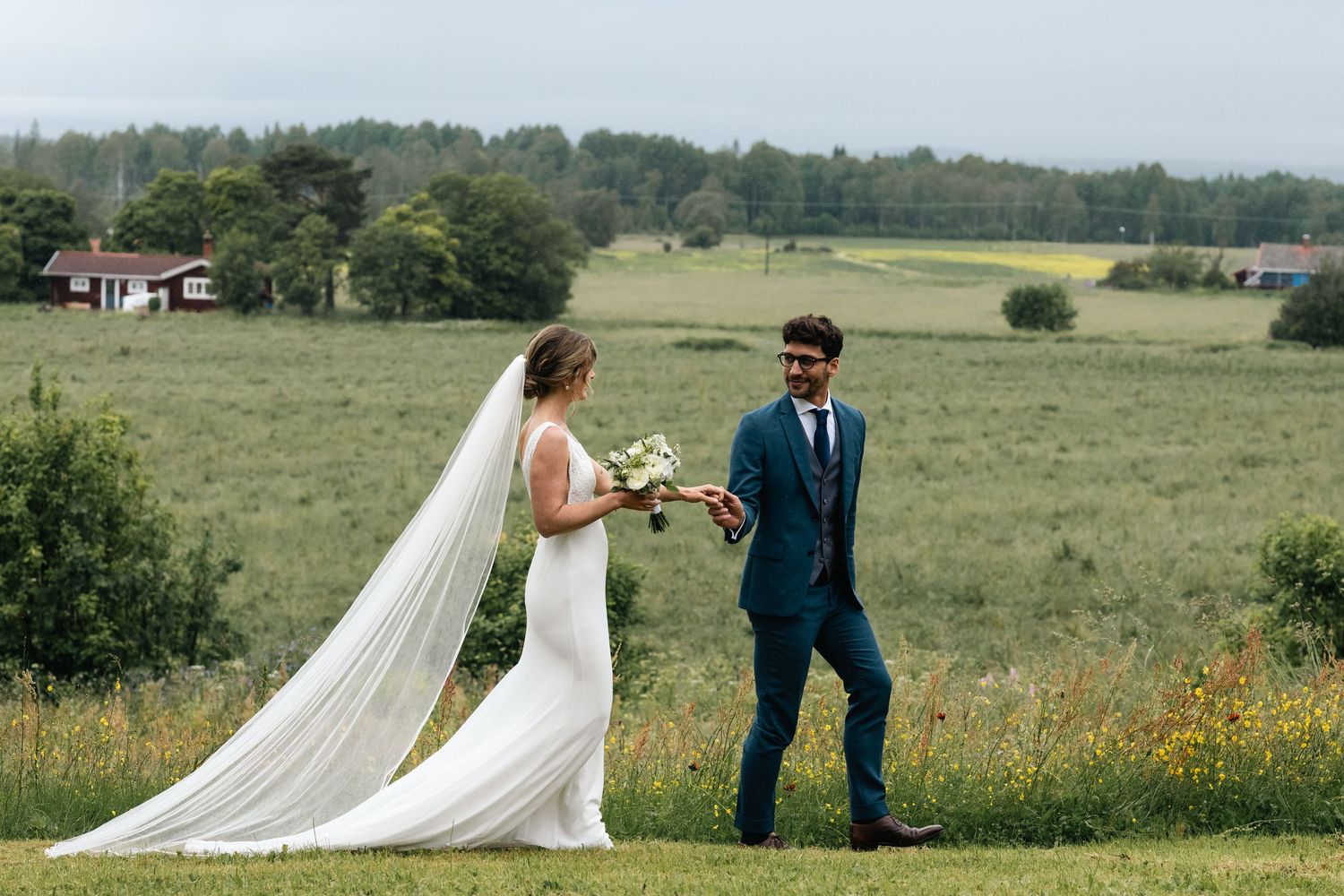 A wedding couple walks through a scenic meadow with rolling hills in the background.
