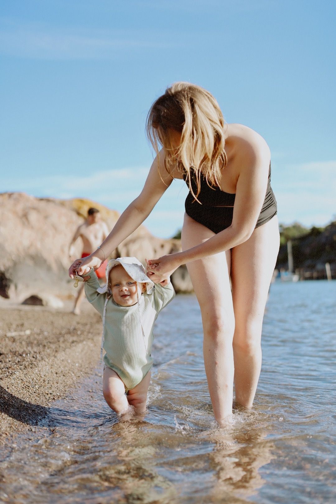 Parent and child playing in shallow beach water on a sunny day.