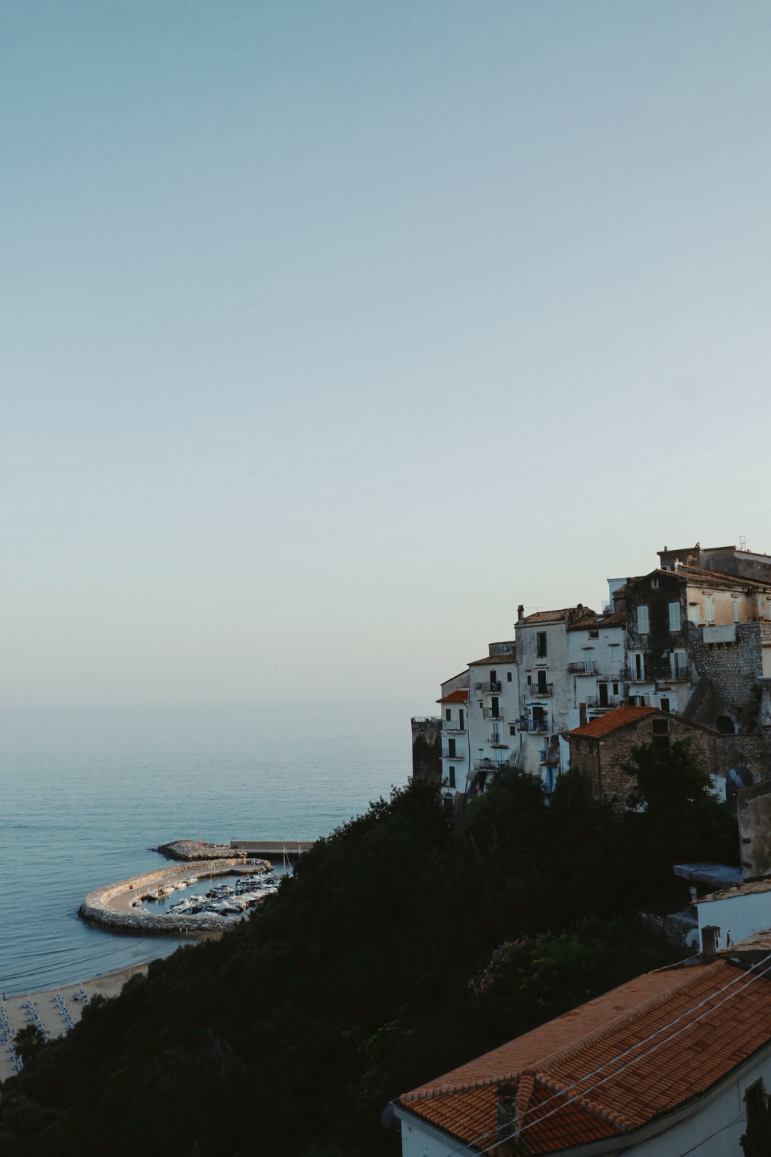 Mediterranean coastal town with white buildings and terracotta roofs overlooking the sea at dusk.