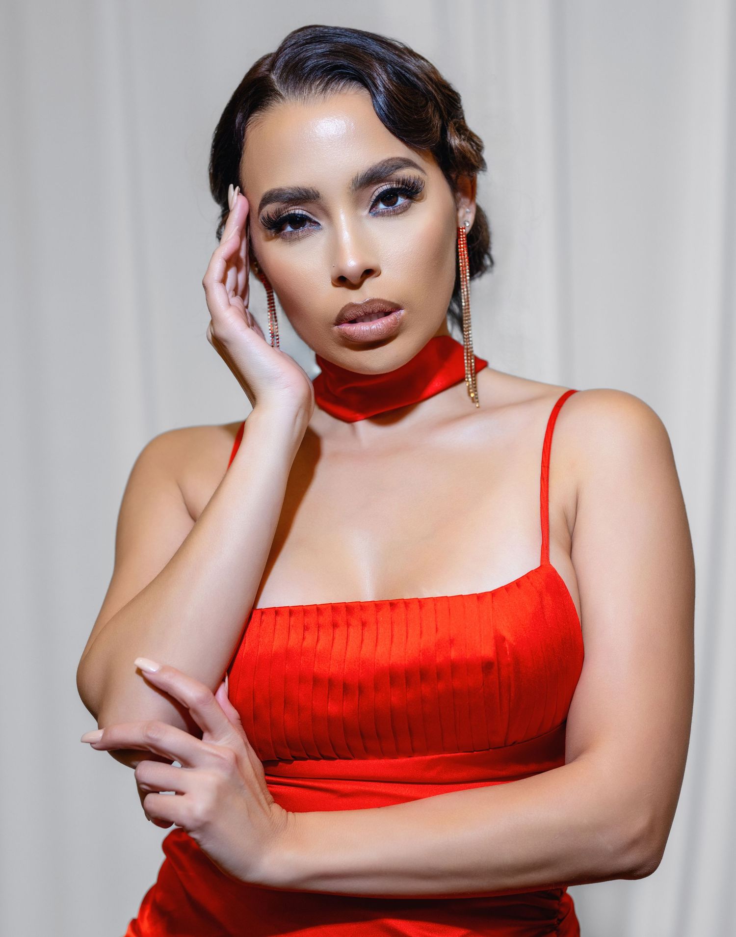 Model in bright red sleeveless dress poses confidently against light backdrop in fashion photoshoot series.