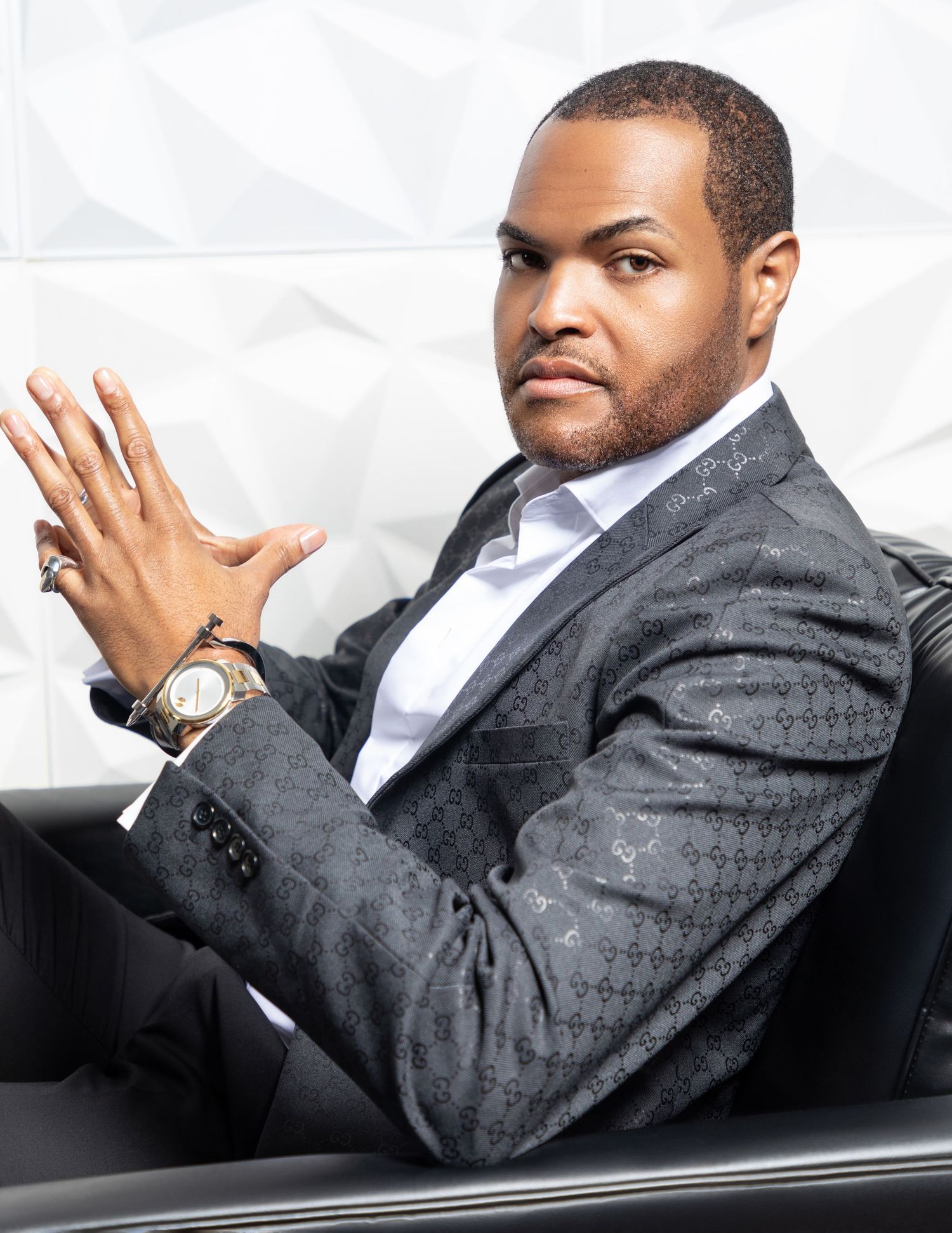 A model in a gray gucci suit sitting in a seat posing with confidence.