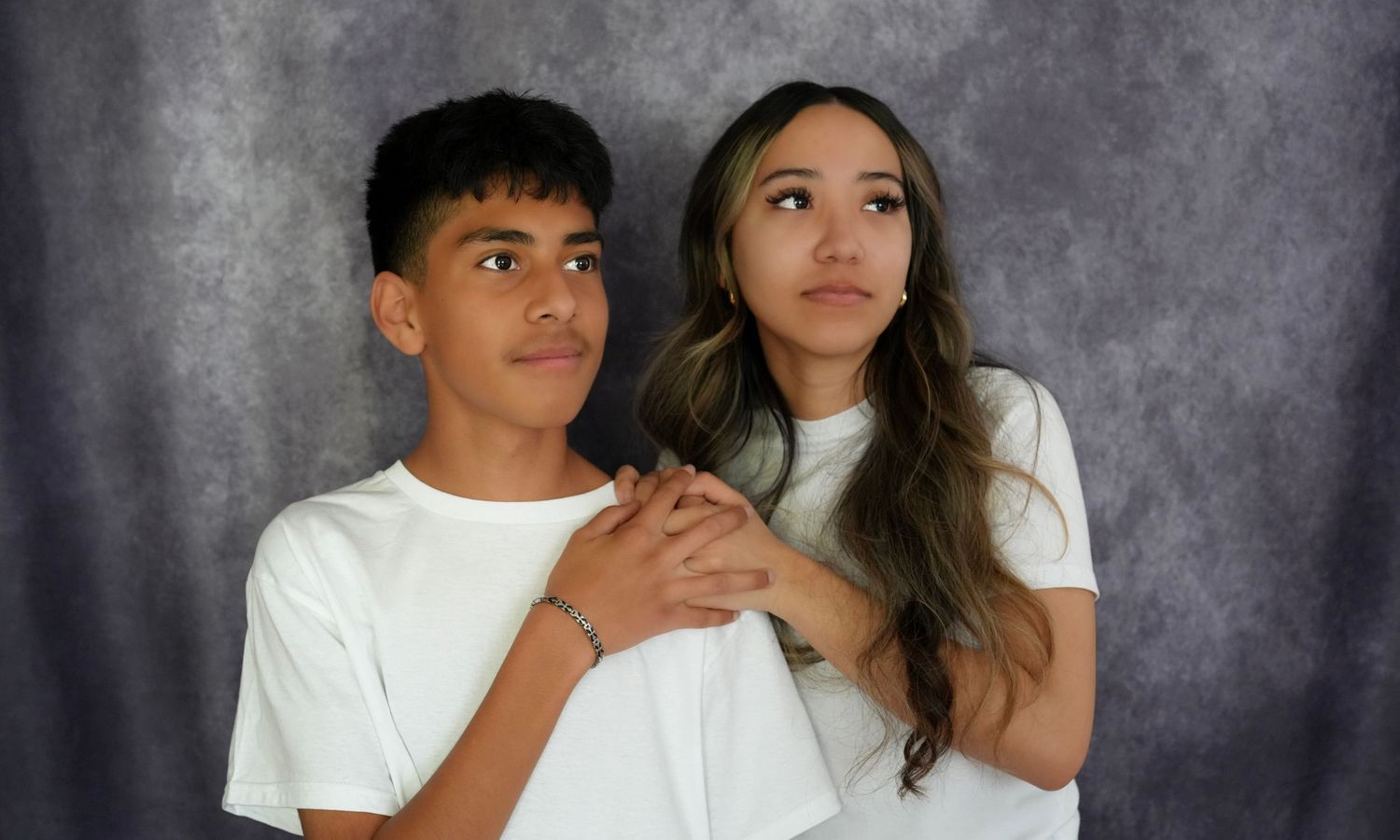 Two young people in white t-shirts pose together against a gray backdrop in a professional portrait photo.