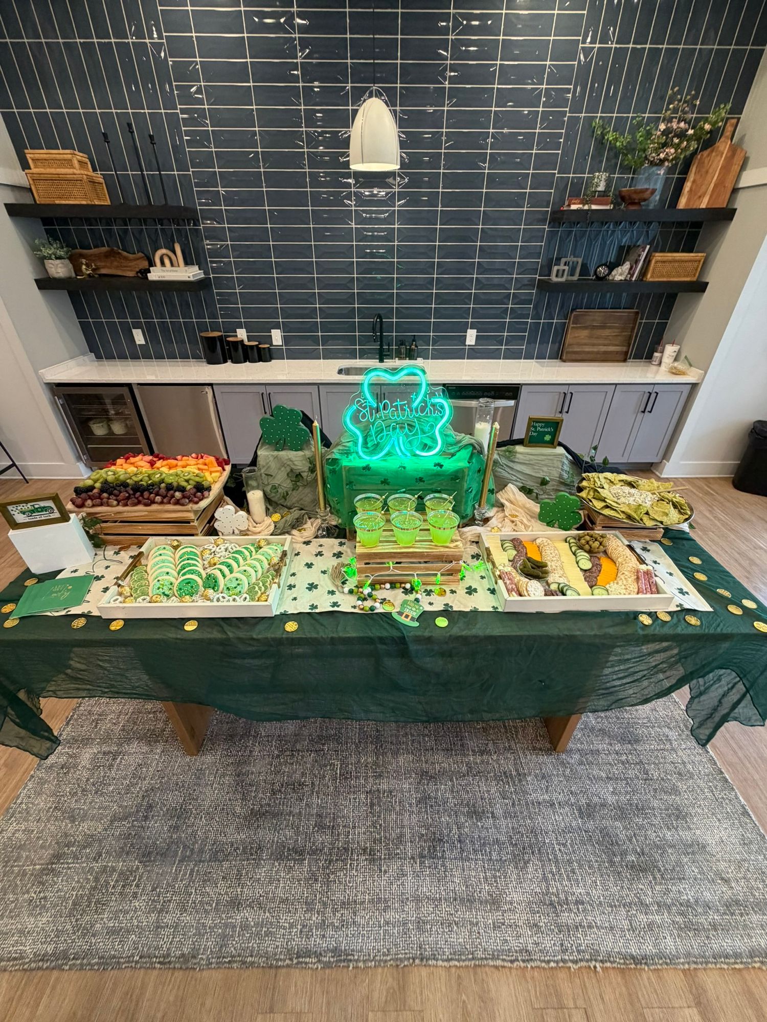 St. Patrick's Day party table with green decorations, shamrock neon sign, and festive food spread on a green tablecloth.