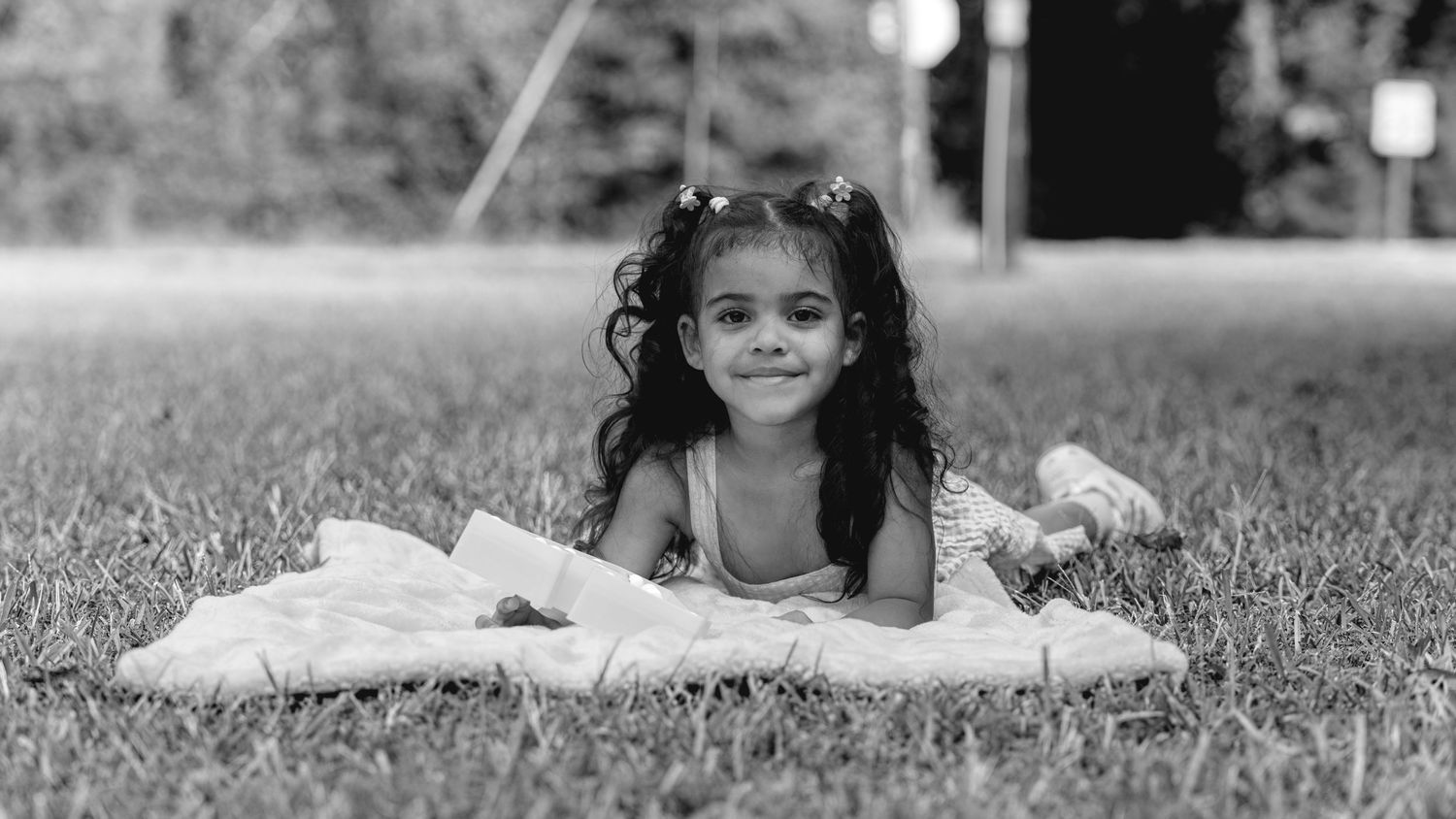 Young girl with curly hair lying on a blanket in the grass, smiling in a black and white photo.