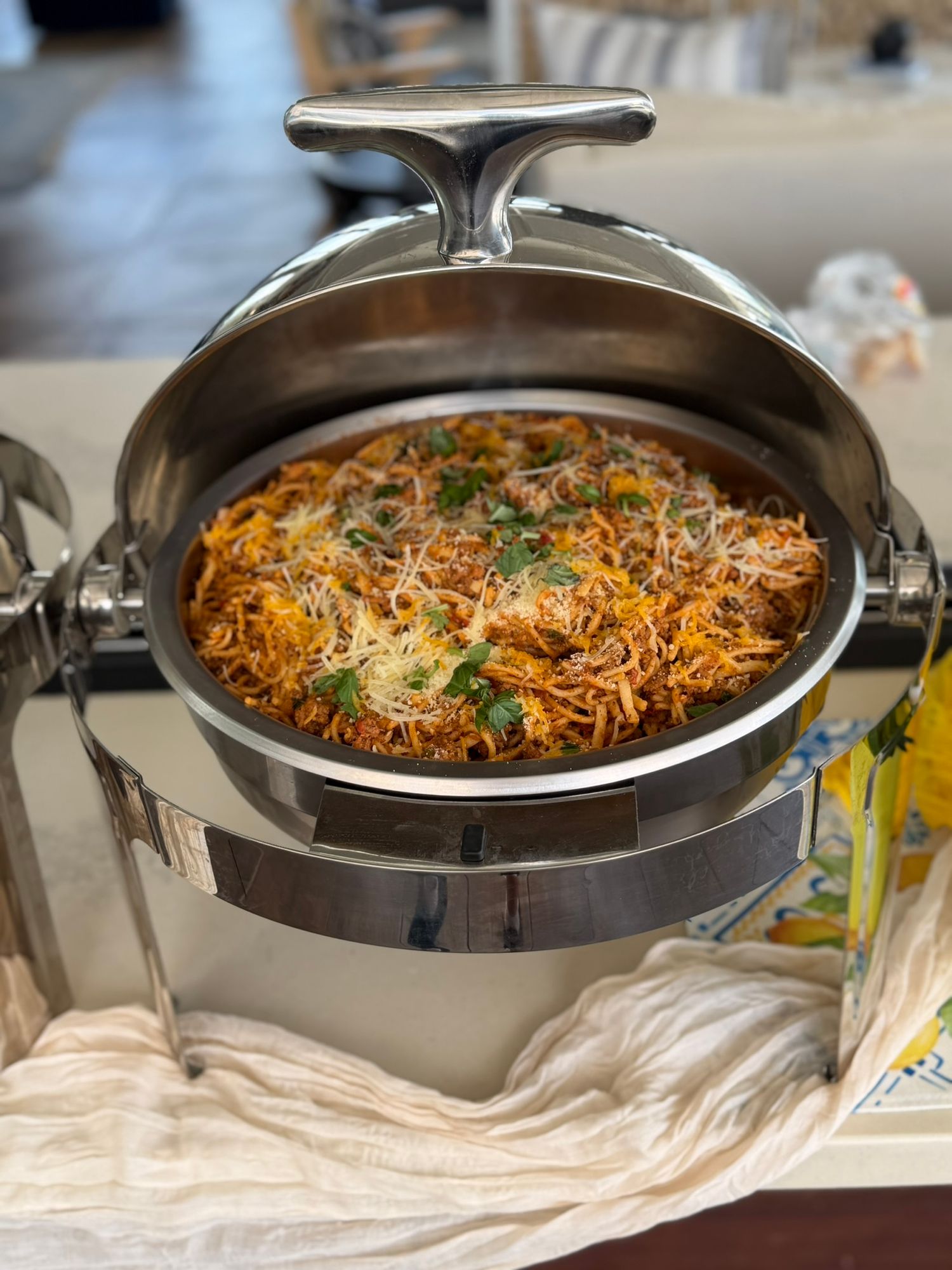 A chafing dish filled with seasoned pasta topped with cheese and fresh herbs at a catered event.