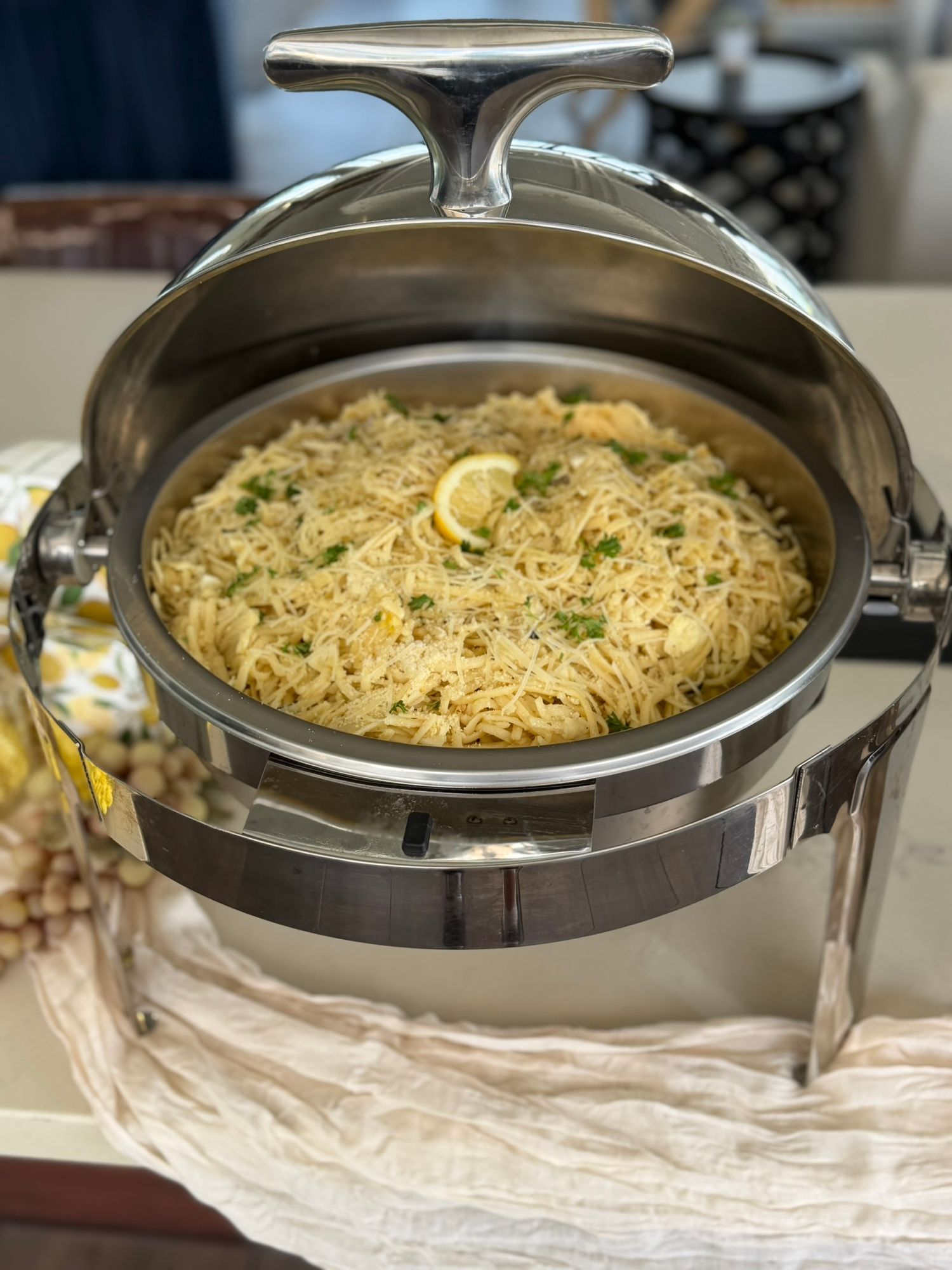 Silver chafing dish filled with lemon herb rice pilaf garnished with parsley and lemon slices at a buffet.