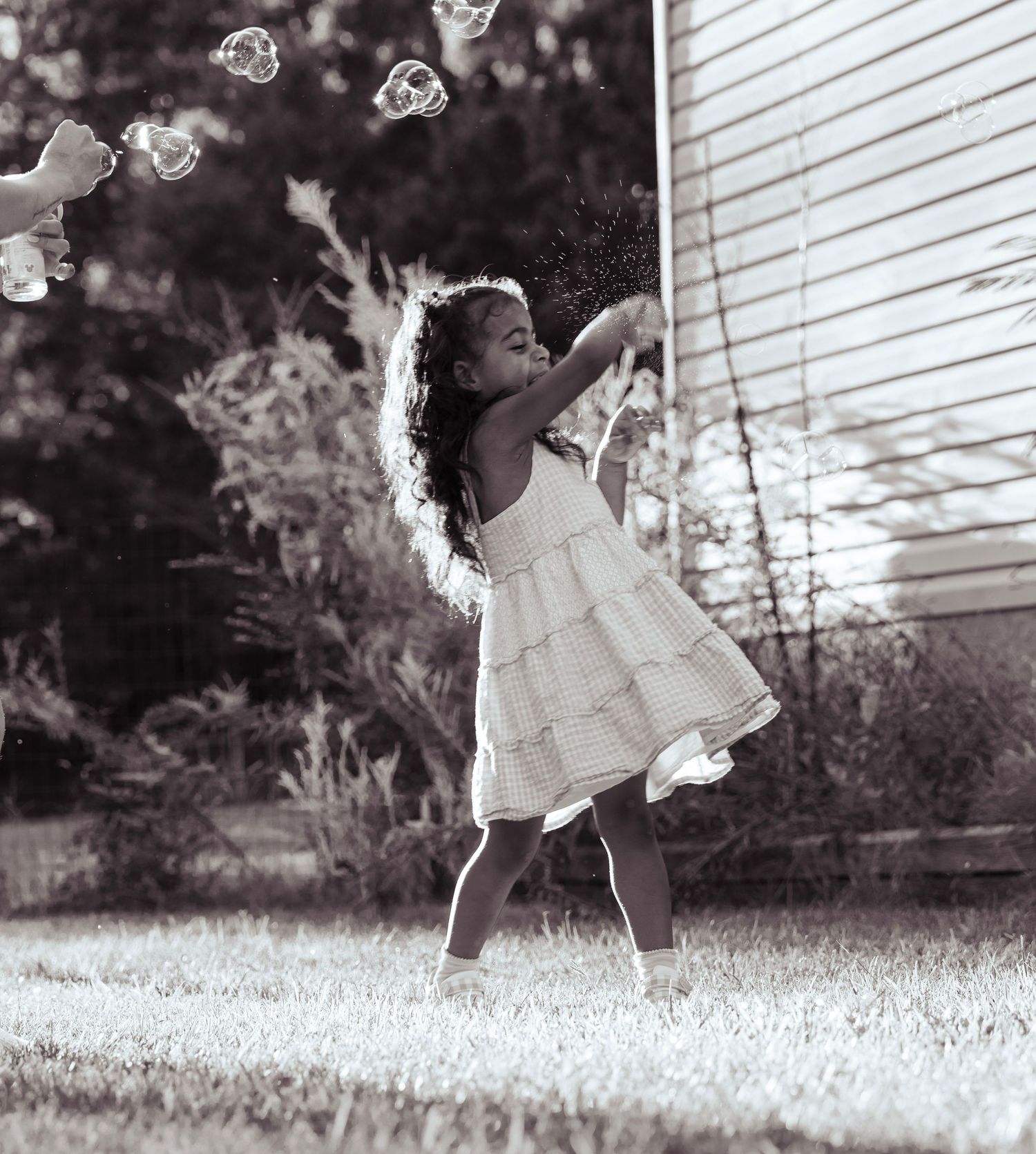 Black and white photo of a girl in a white dress joyfully catching bubbles outdoors.