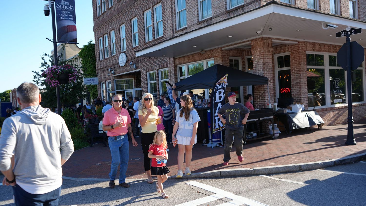 People strolling on a sunny brick sidewalk outside a charming brick storefront in a small downtown shopping district.