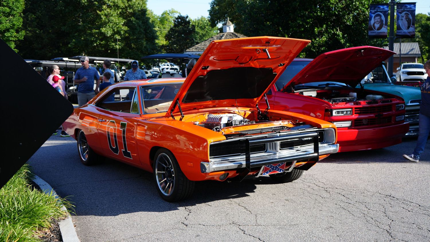 Orange General Lee Dodge Charger with hood open at a classic car show outdoor event.