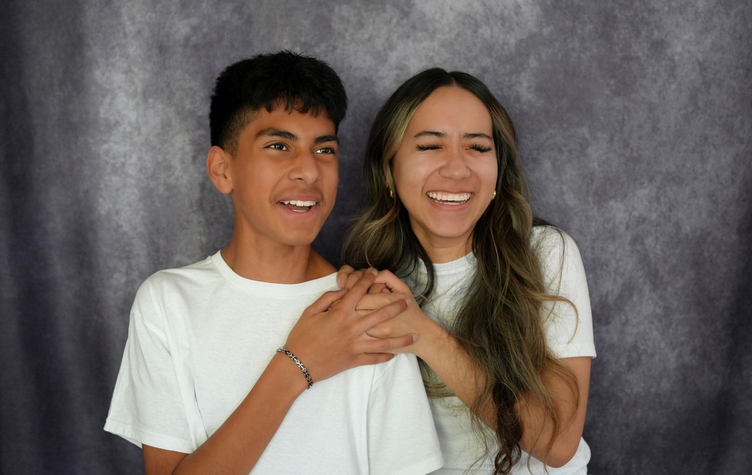 Two smiling young people in white t-shirts posing together against a gray backdrop.