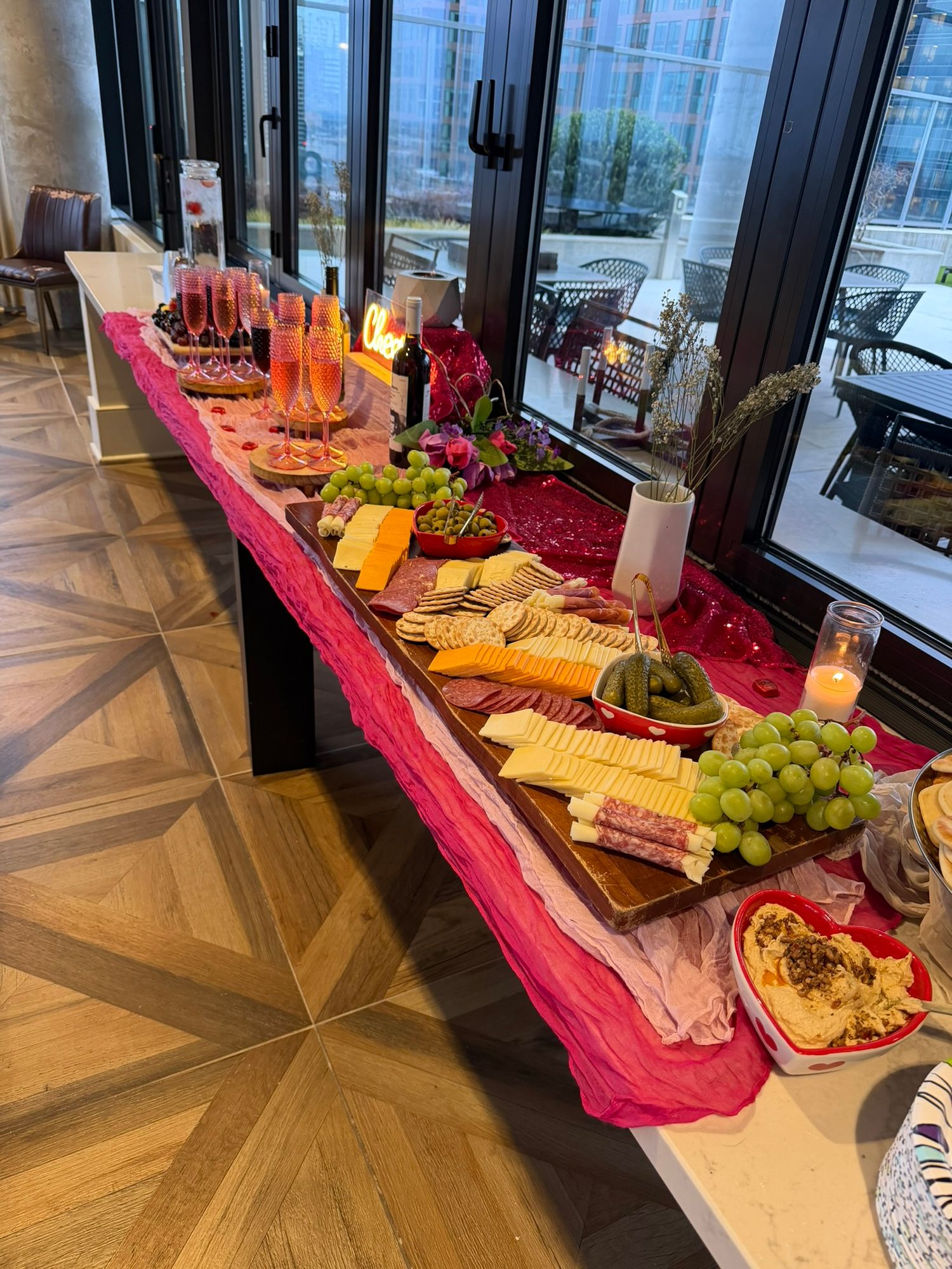 Elegant charcuterie board spread with cheese, grapes, and dips on a long table with pink runner and candles.