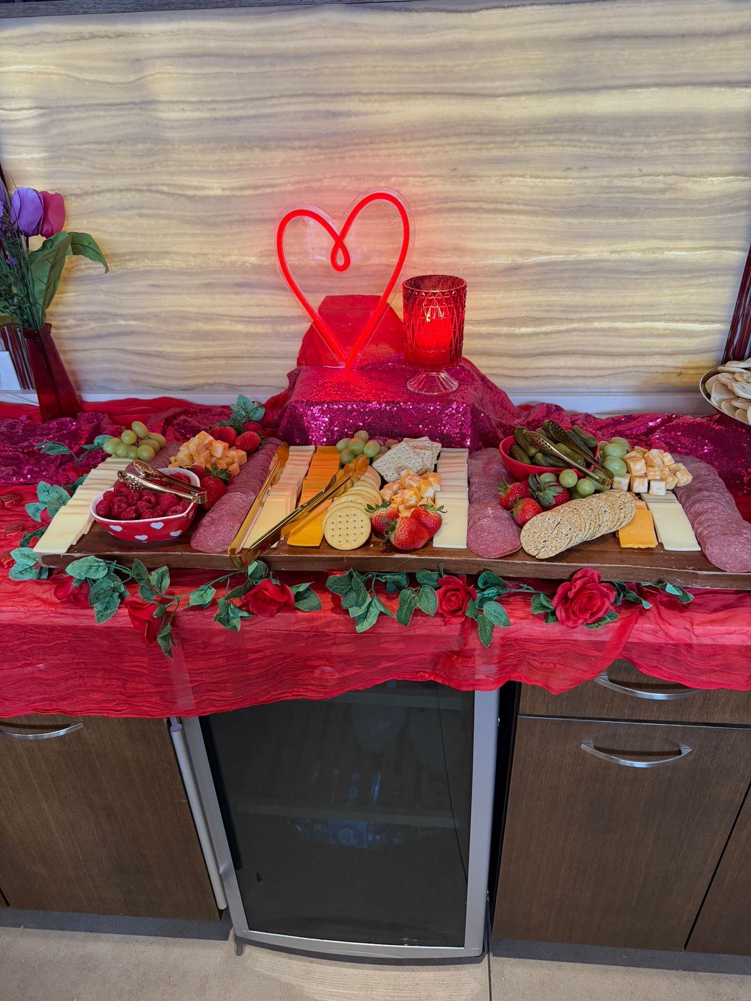 Valentine's Day charcuterie board with cheese, fruits, and crackers on a red sequin tablecloth with heart neon light.