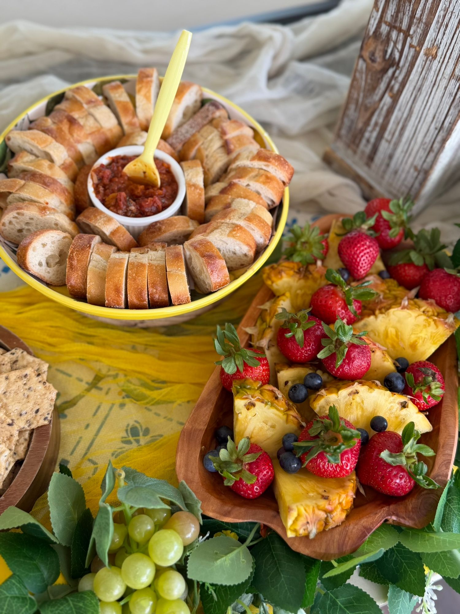 A colorful spread featuring sliced bread with salsa dip, fresh strawberries, pineapple chunks, blueberries, and green grapes.