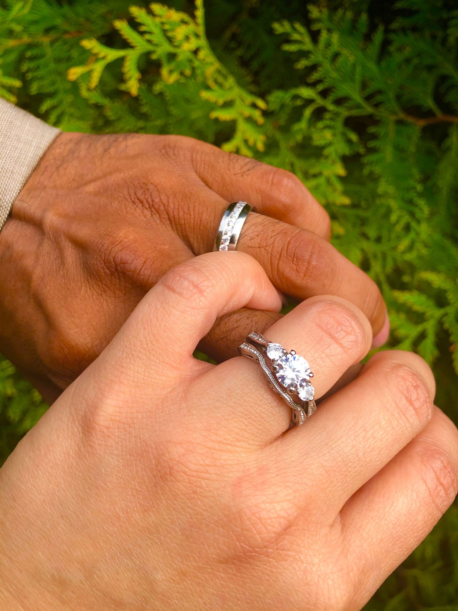 A sparkling diamond engagement ring shown in multiple angles on a hand against a green leafy background.