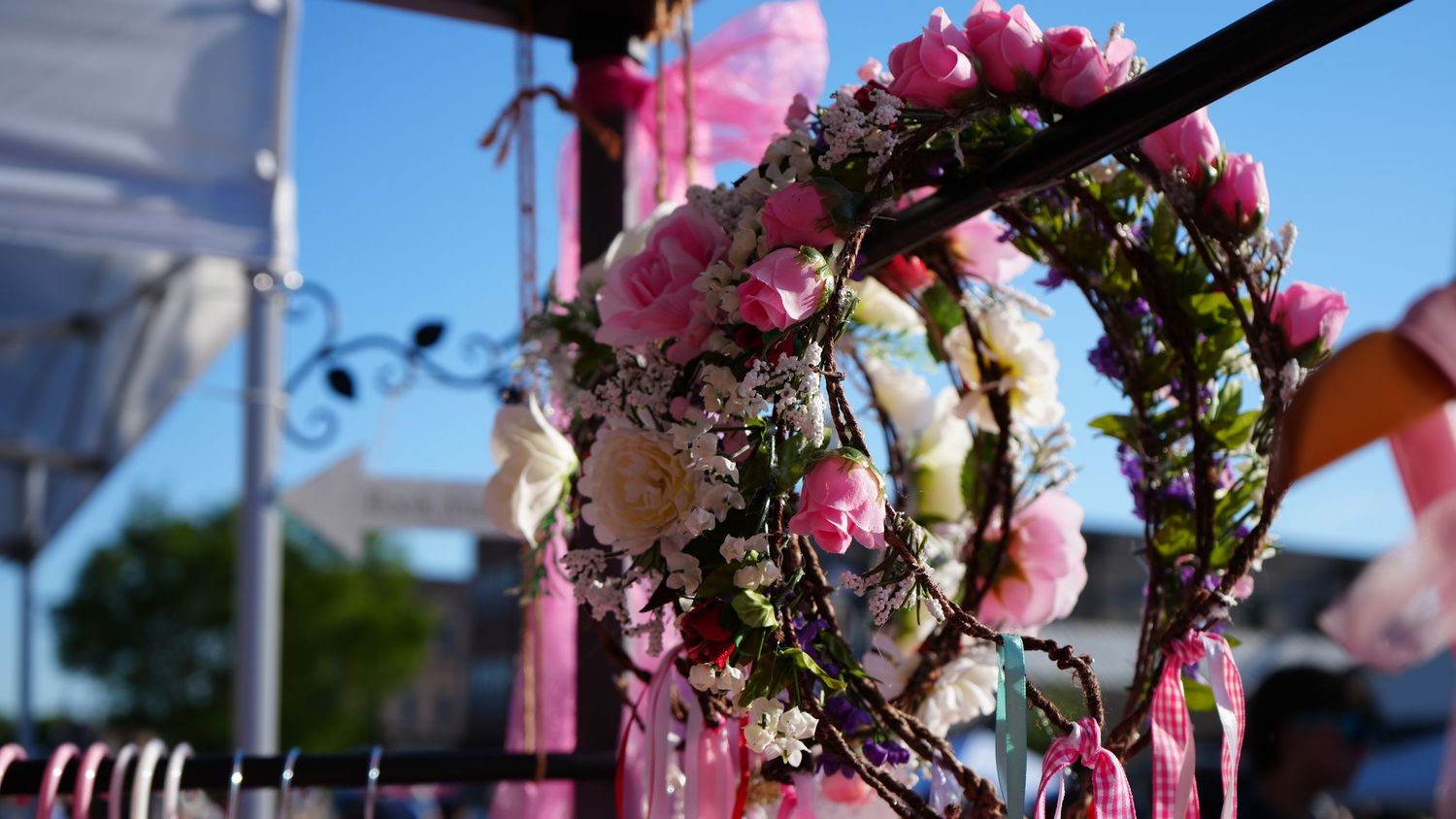 Pink and white floral wreaths with ribbons hang outdoors under a blue sky at a festive event.