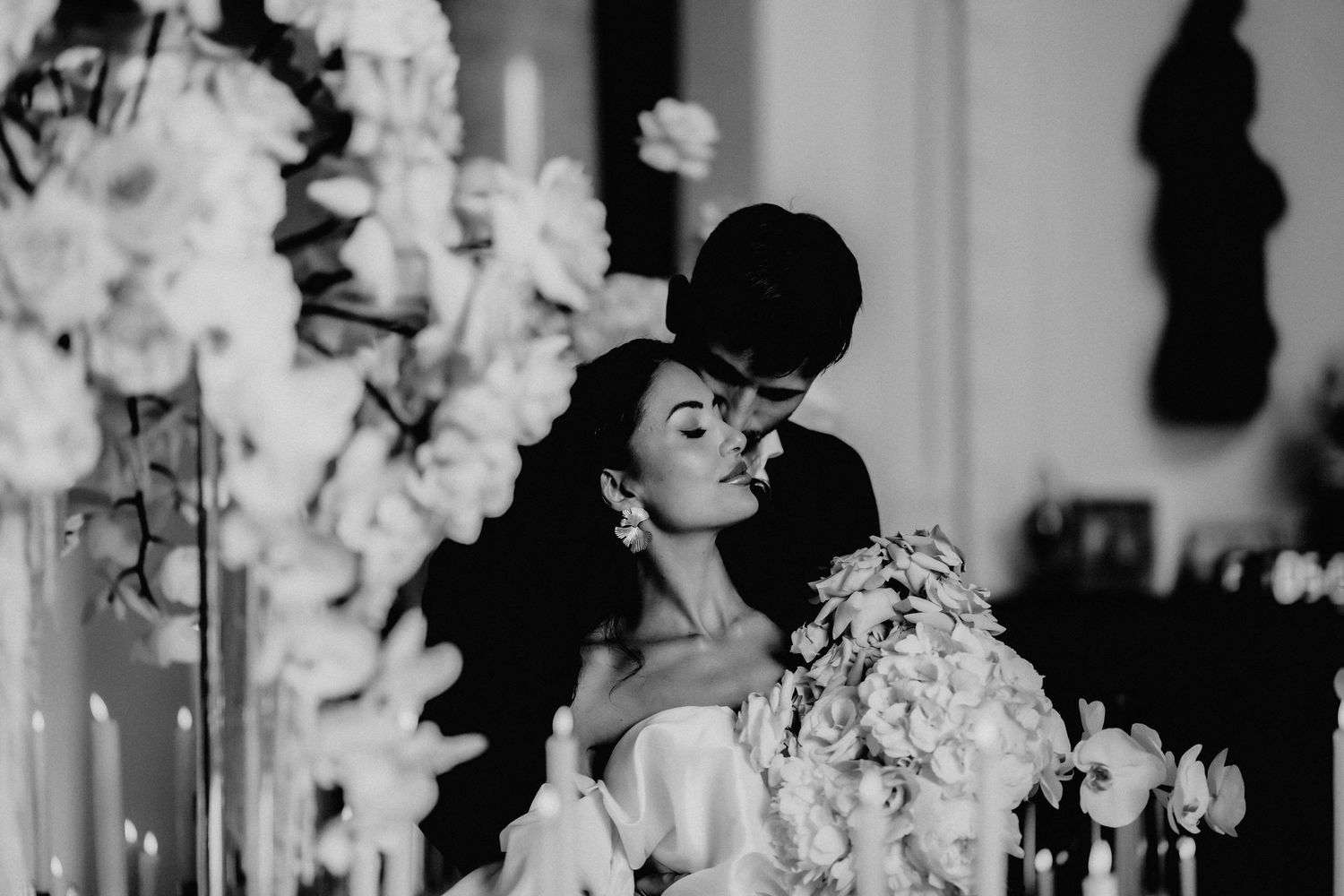 A black and white wedding photo showing a couple dancing intimately at their reception with floral decorations.
