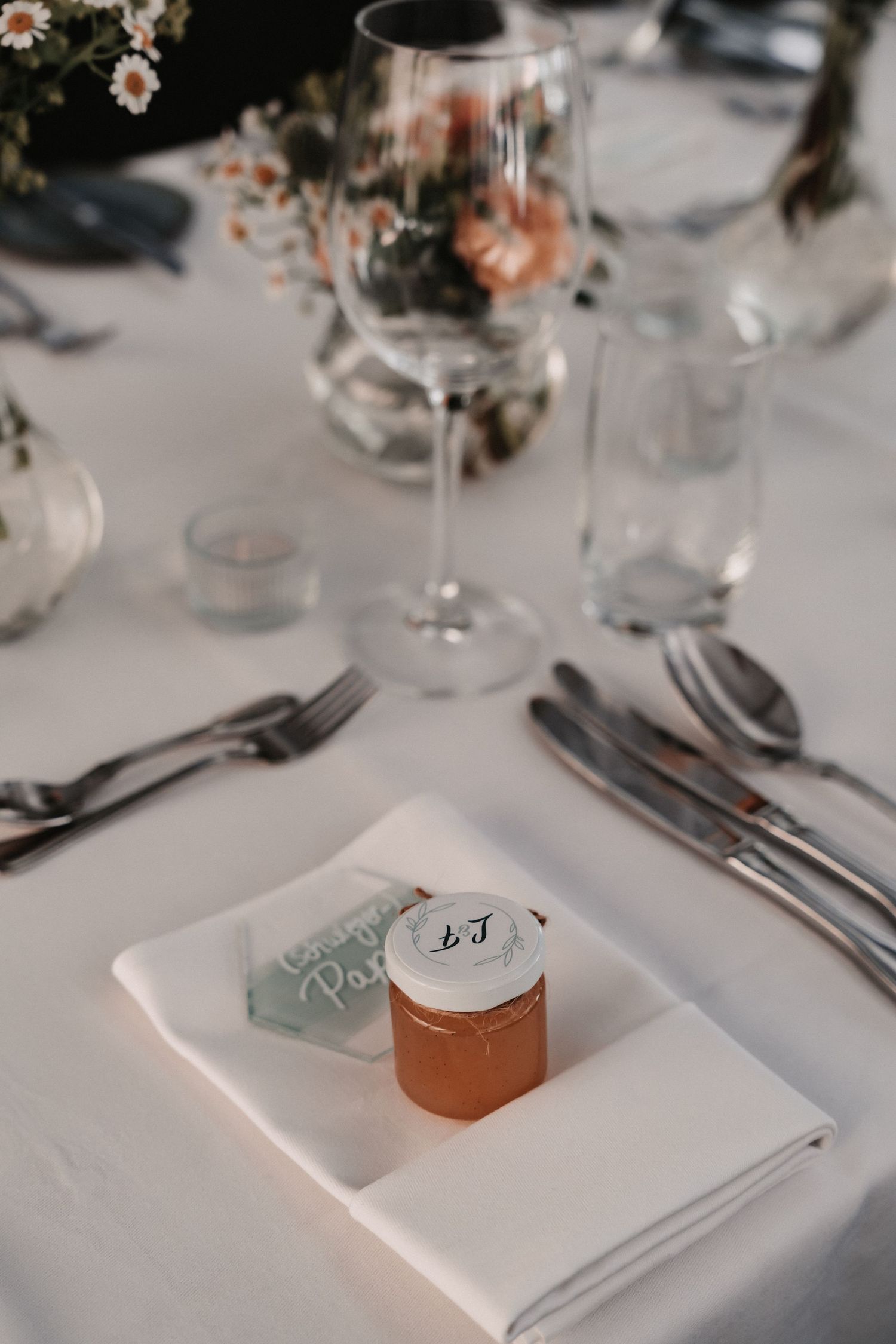 Elegant wedding table setting with wine glass, silverware, white napkin and small jar of honey as a wedding favor.