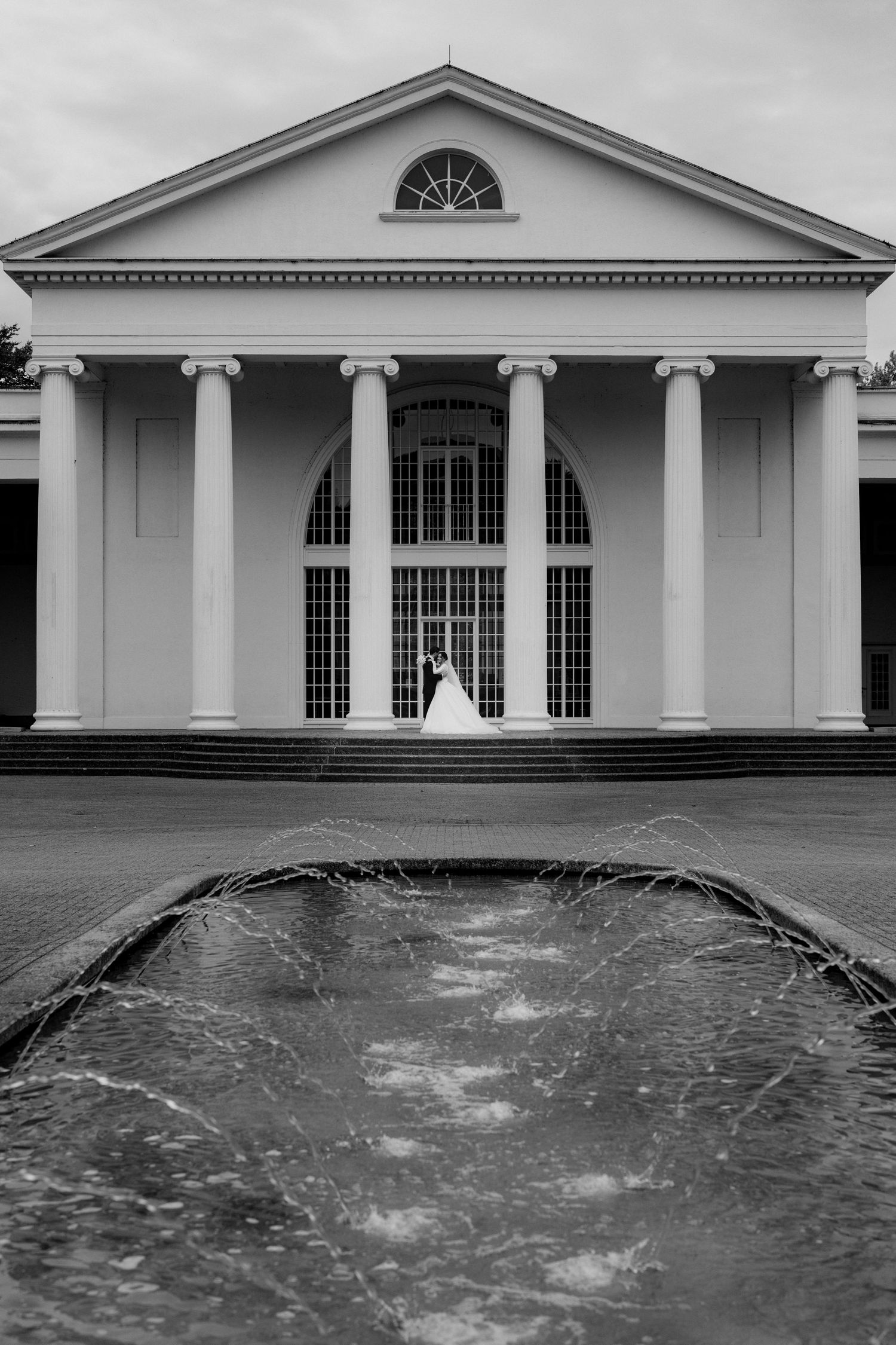 Classical white building with columns and reflecting pool creating a symmetrical architectural scene.