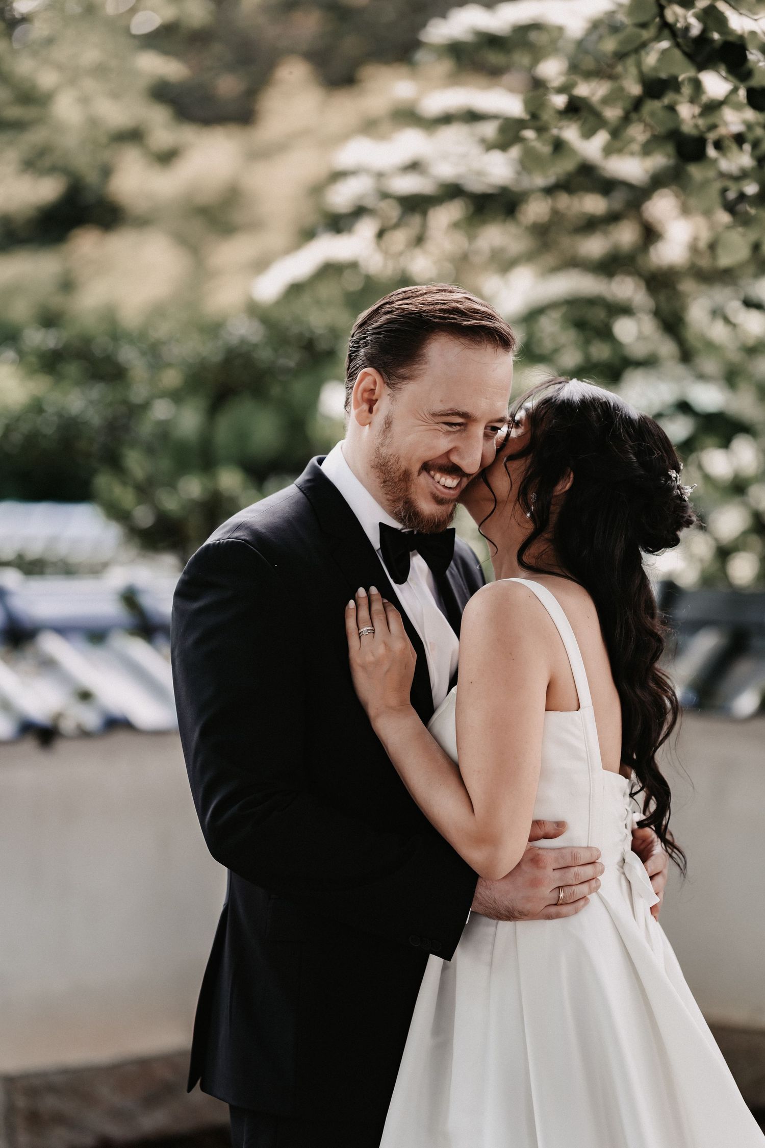 A romantic moment between newlyweds sharing a laugh together outdoors in their wedding attire.