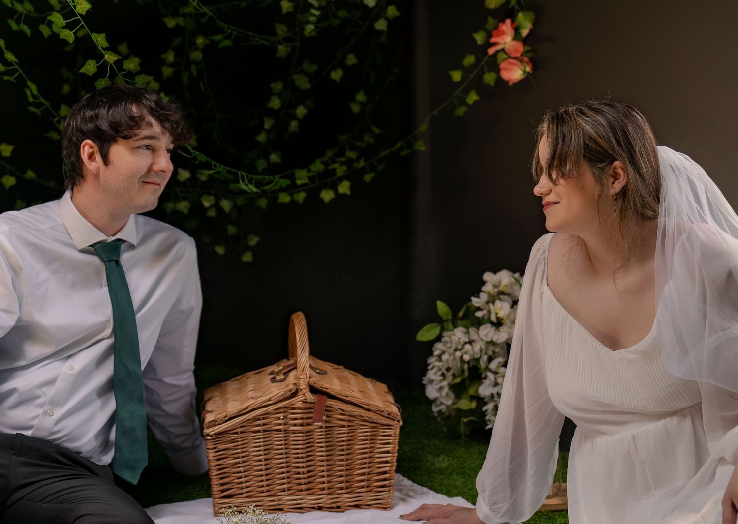 Bride in white veil and groom in green tie share a romantic glance at outdoor picnic wedding setting.